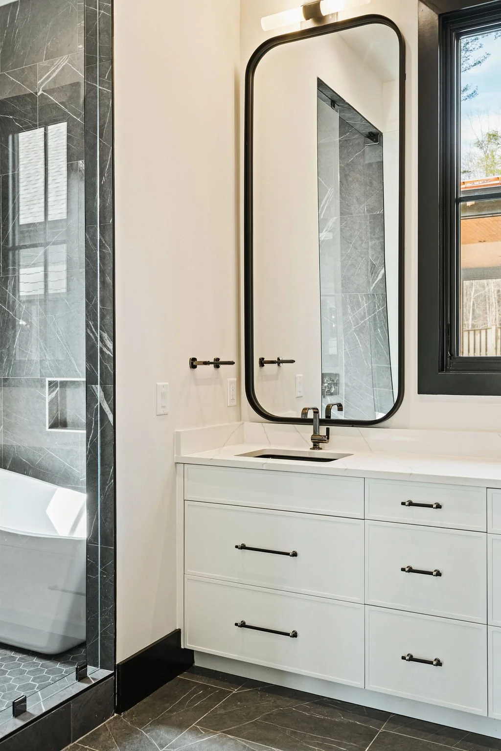 Brightly lit modern bathroom with large mirror and white cabinets.