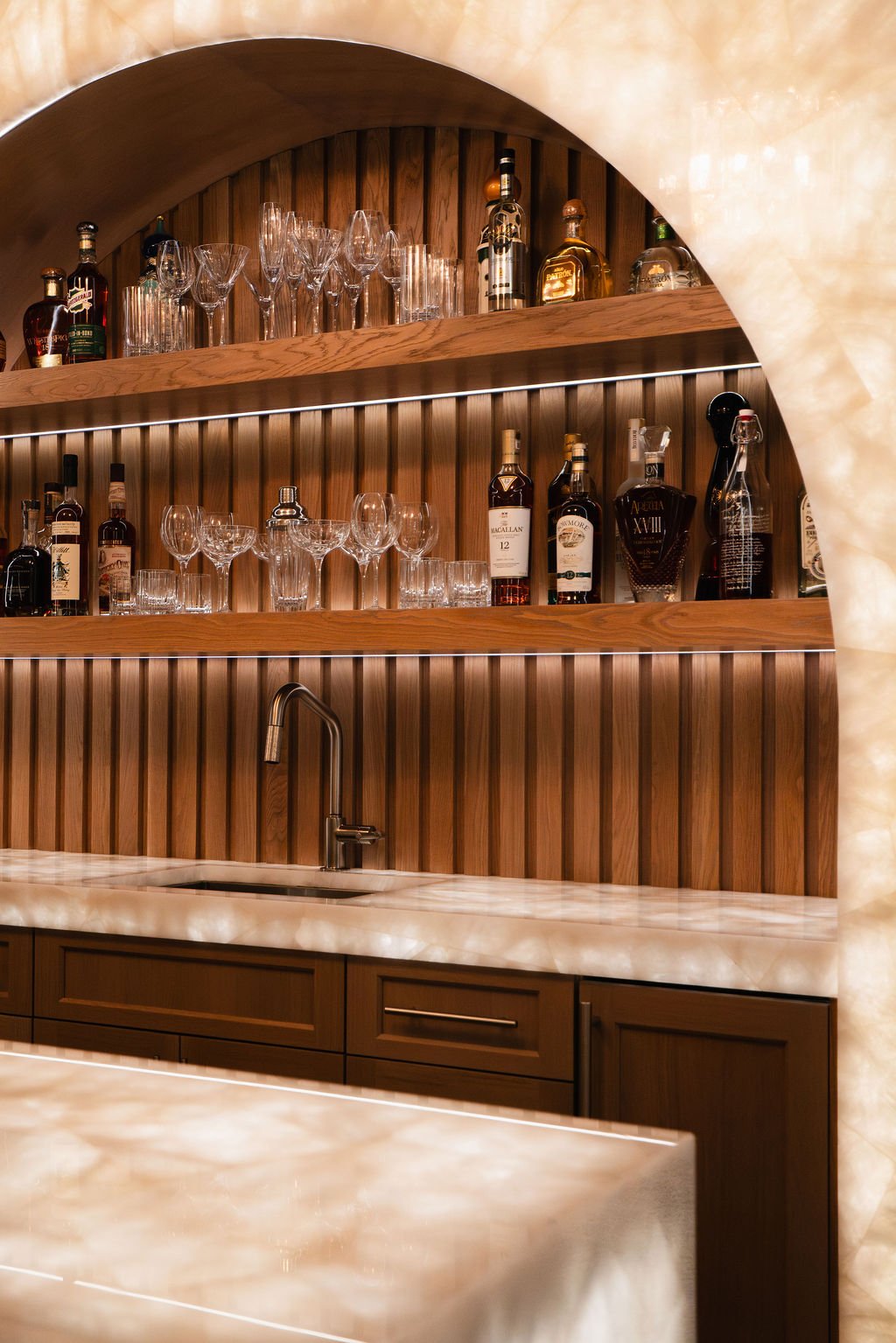 Custom home bar with illuminated marble, arched wood shelving, integrated lighting and built-in cabinetry.