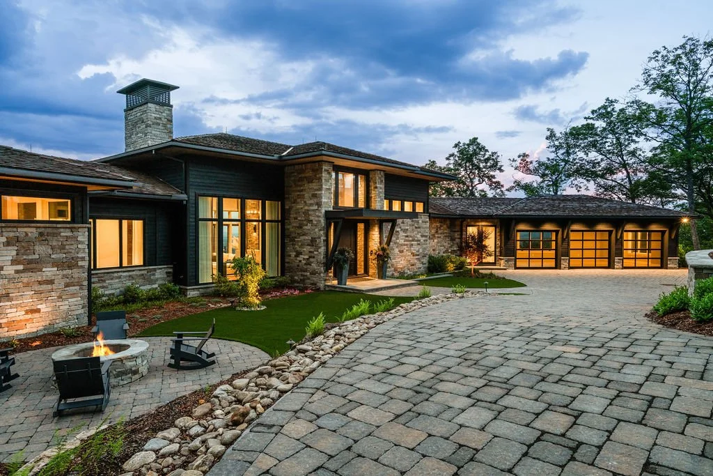 Modern, luxury home at twilight with stone driveway, fire pit and three car garage.