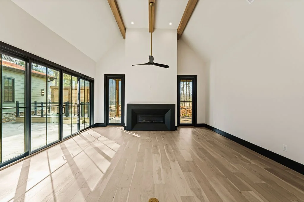 Open living room with wood beams, fireplace and large windows looking into a courtyard.