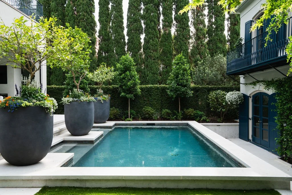 Private courtyard with a modern swimming pool, oversized planters, formal landscaping and black-trimmed balconies.