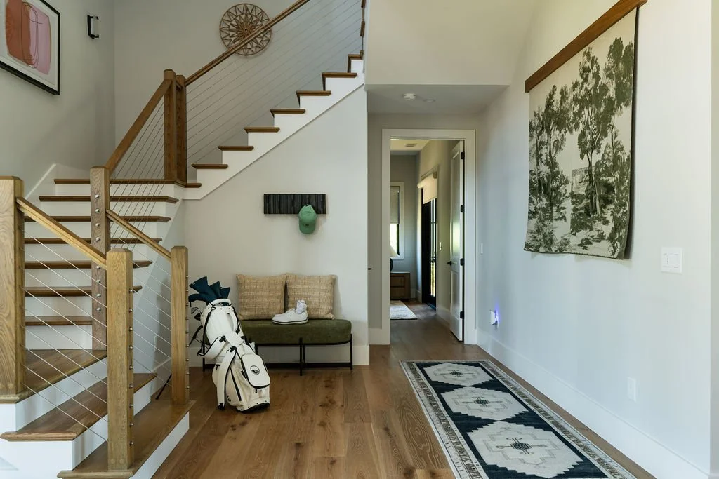 Foyer of home golf bag, seating area, rug, art and a doorway leading to a bedroom and a staircase leading up on the other side.
