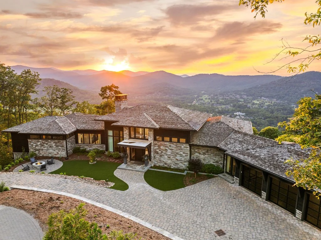 Aerial sunset view of a luxury stone mountain home with a three-car garage, landscaped courtyard and panoramic mountain views.