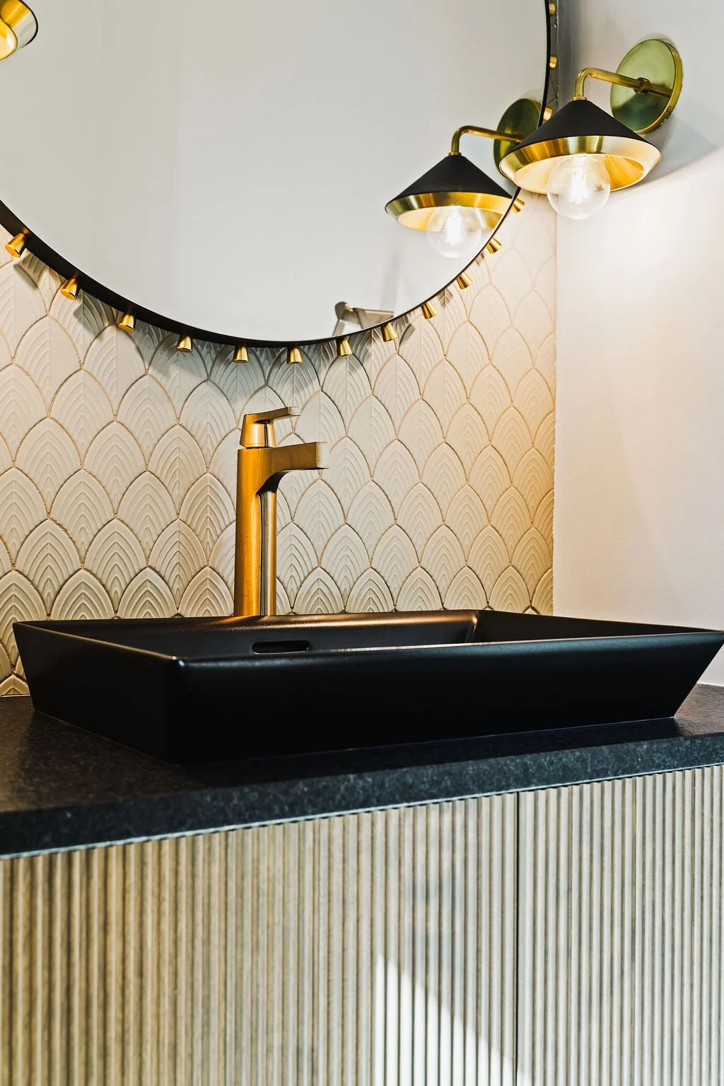Modern, luxury black bathroom sink with gold faucet and pendant light.