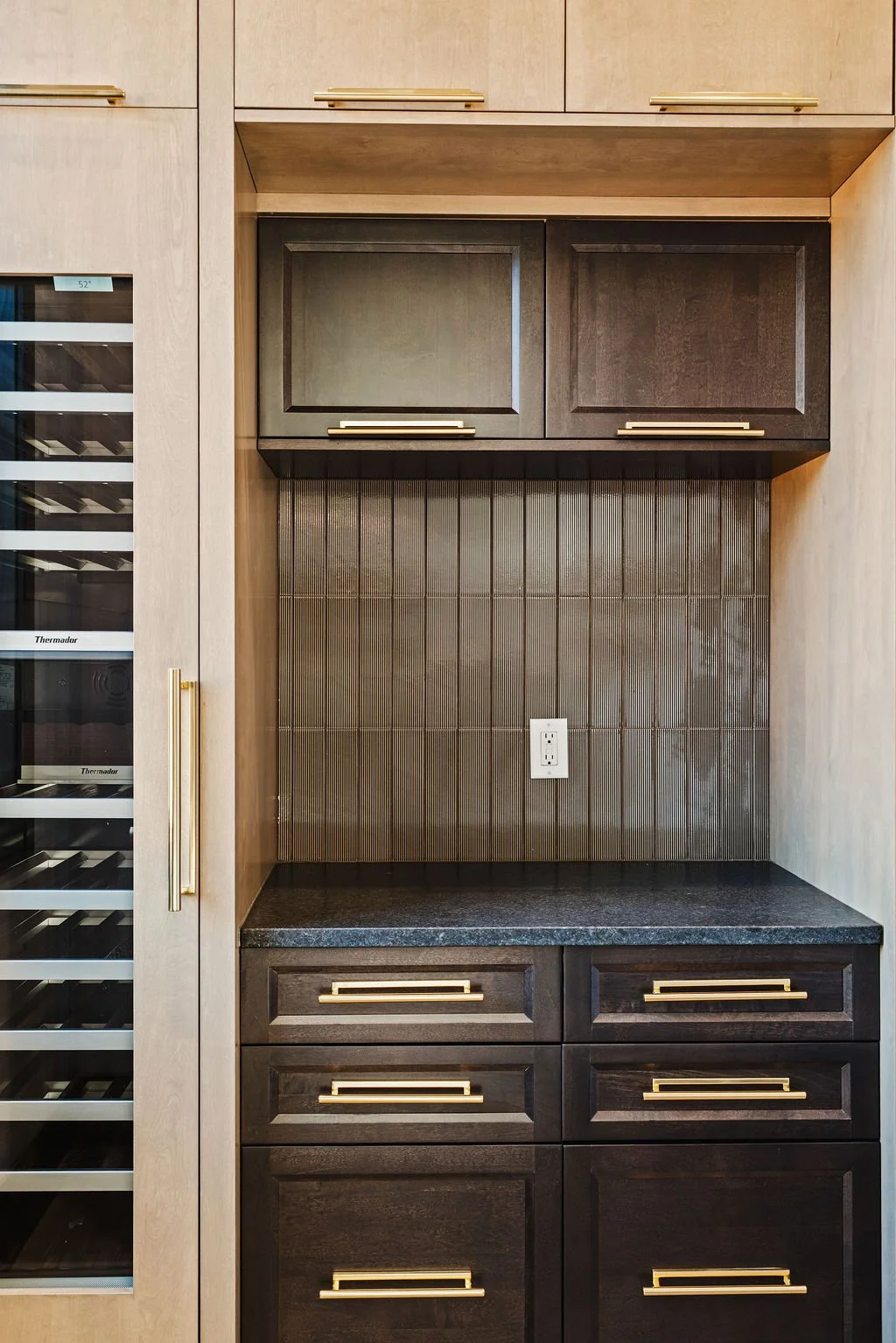 Beige wood wine pantry with dark colored granite countertop and walnut colored cabinets.