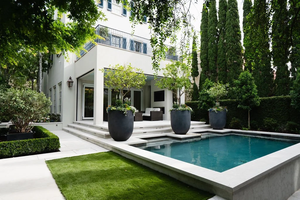Private courtyard with a modern swimming pool, covered patio, white stucco exterior, manicured landscaping and oversized planters.
