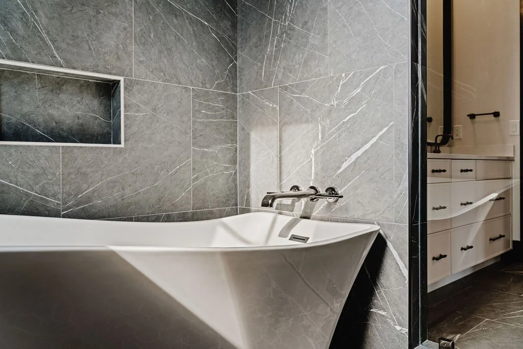 Close-up of bathtub with marbled tile on the wall and cabinetry in the background. 