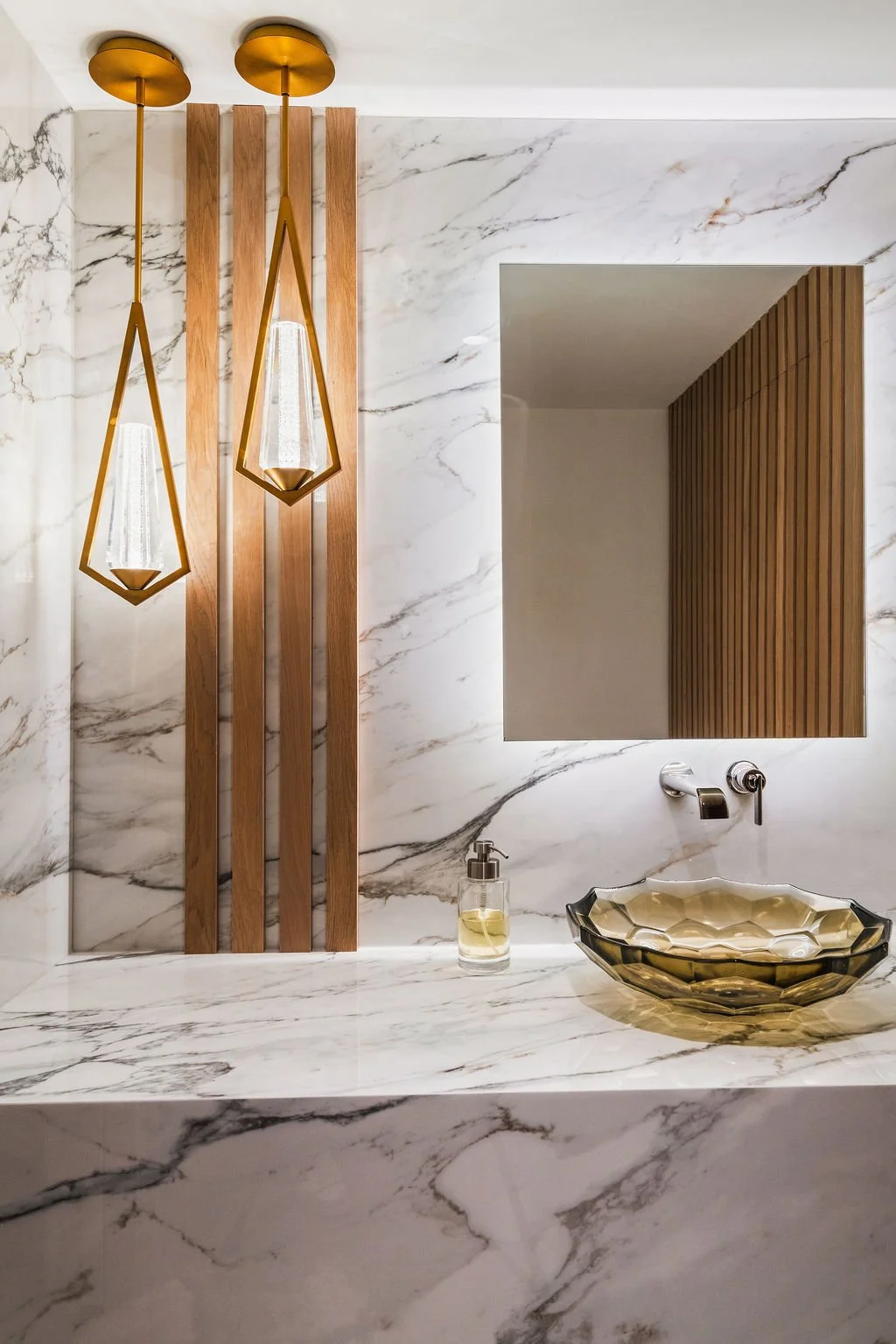 Luxury Charleston powder room with marble walls, sculptural glass sink, brass pendant lights and vertical wood detailing.