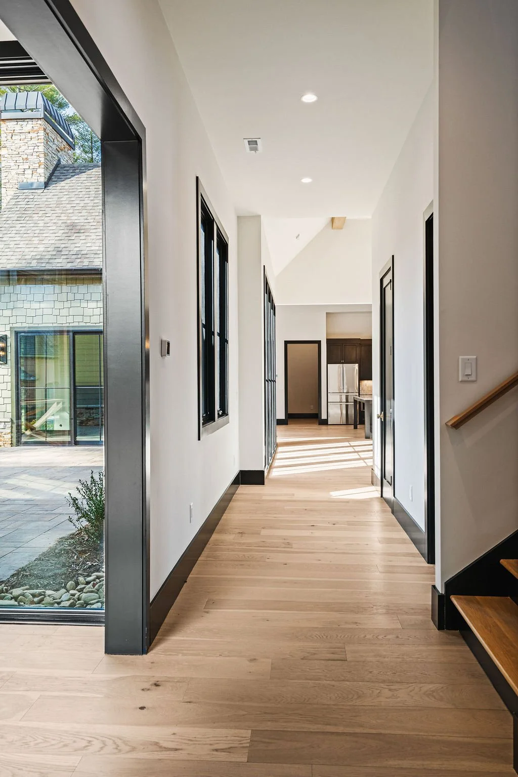 Long hall way leading to open floor plan with light pouring in through large windows on one side of the hall.