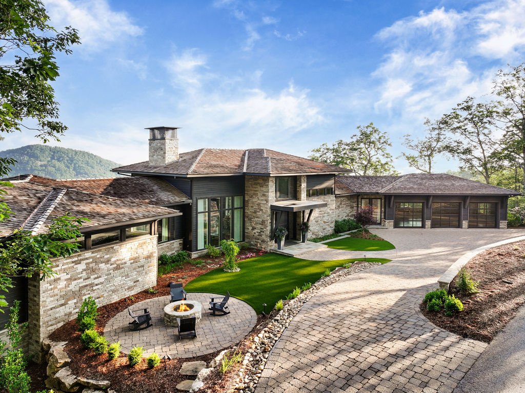 Elevated exterior view of a luxury mountain home with stone siding, wood accents, a three-car garage and Blue Ridge views near Asheville, North Carolina.