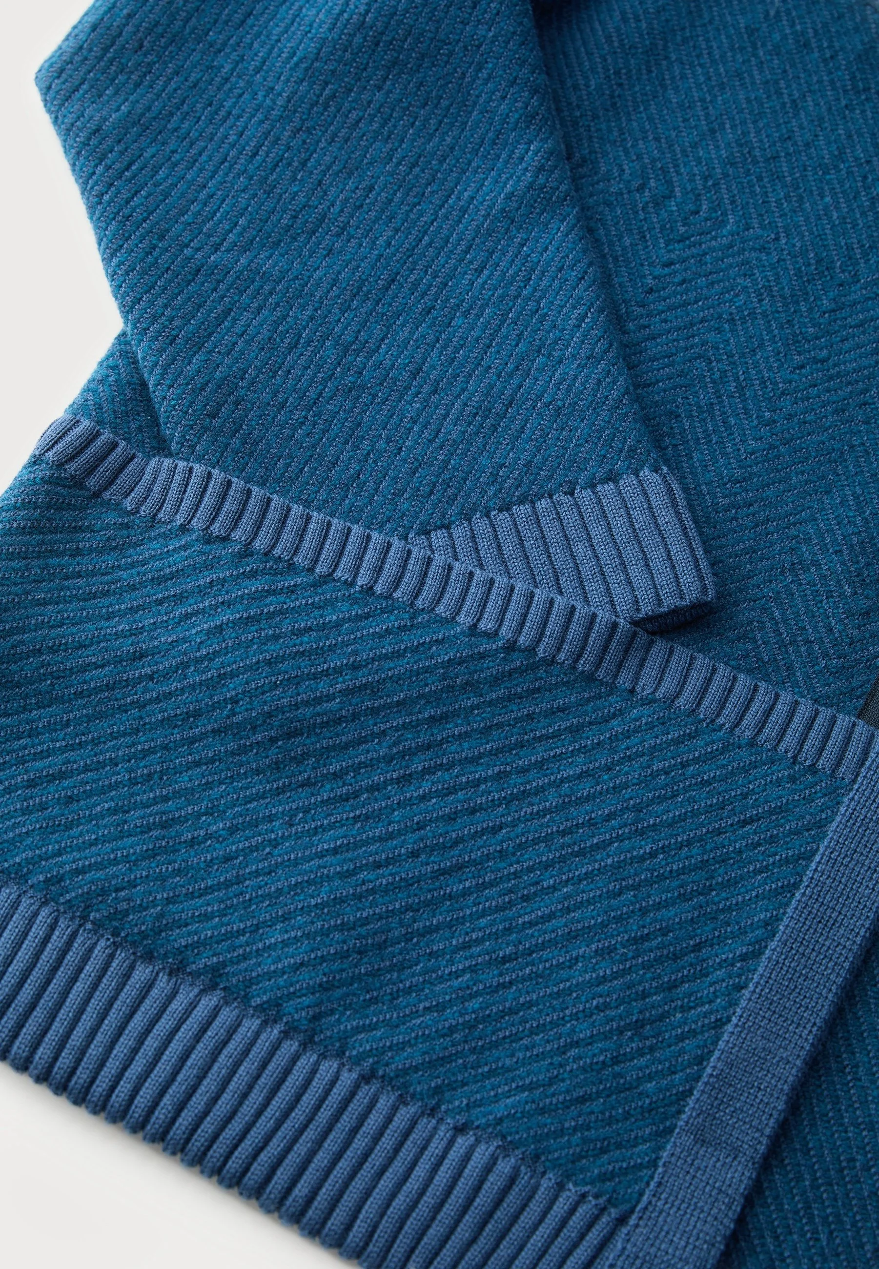 Close-up of a folded blue knit sweater with ribbed cuffs and collar.