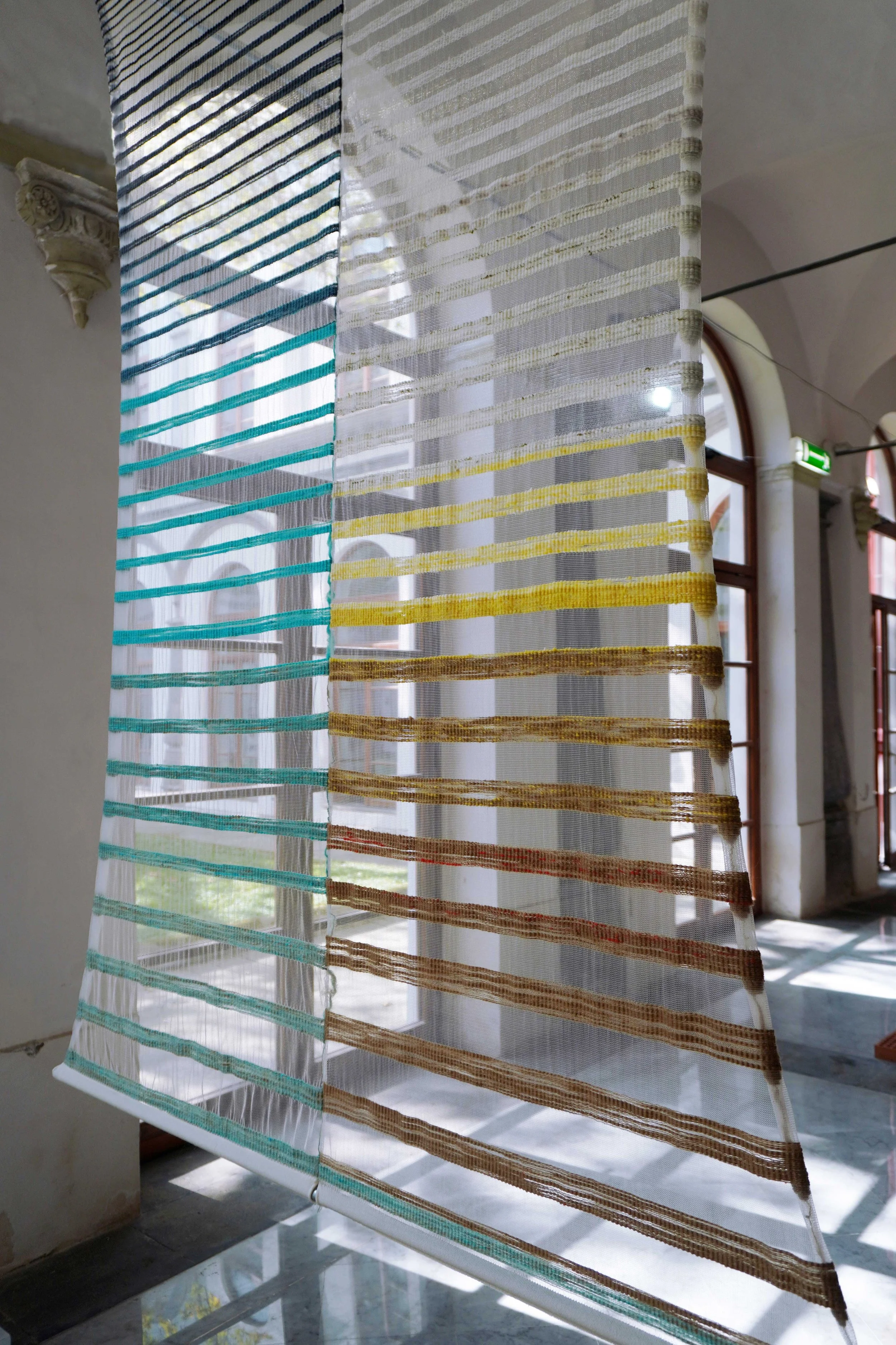 Colorful sheer curtain with multicolored horizontal stripes hanging in a bright room with arched windows.