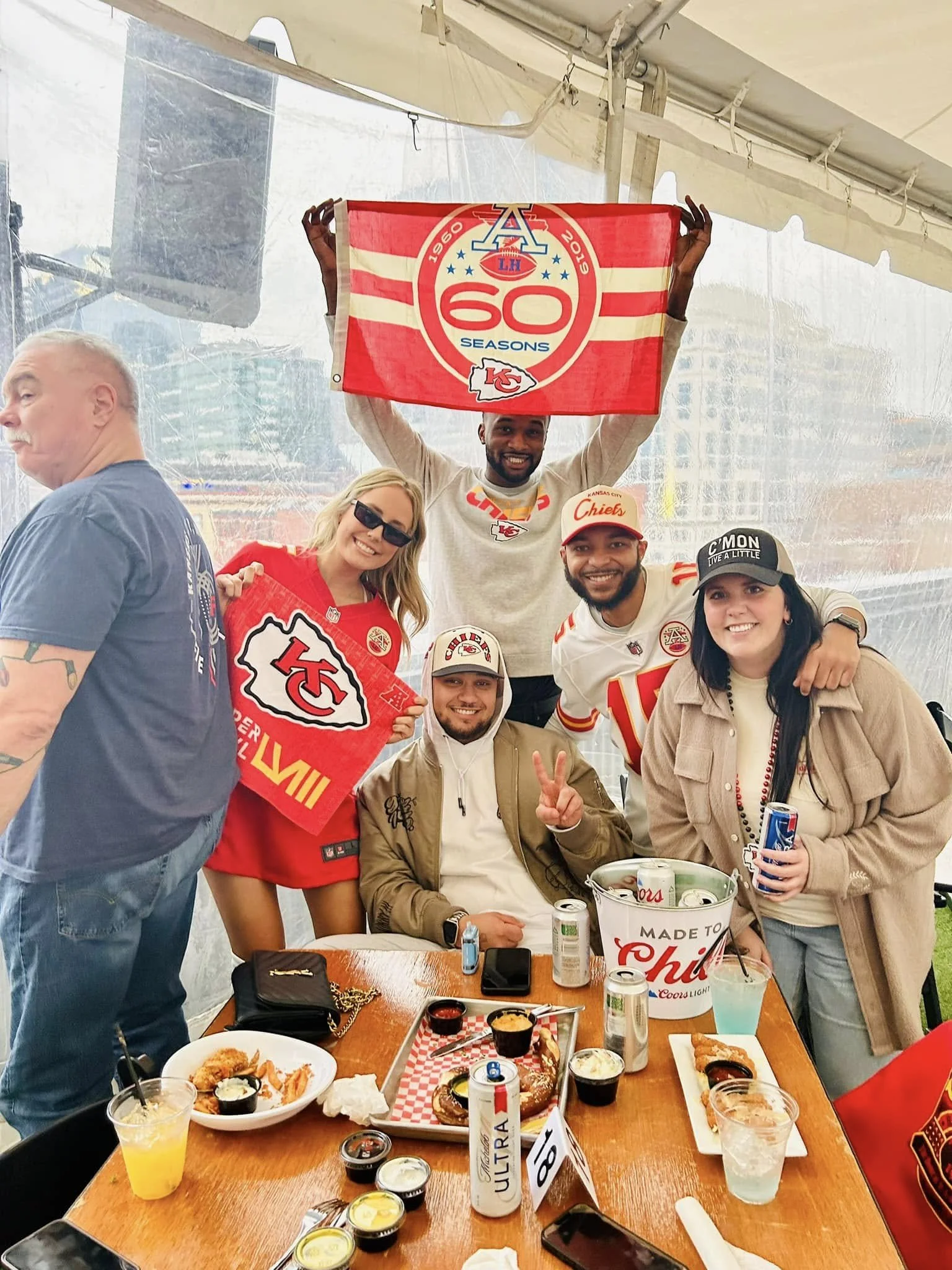 A group of people celebrating at a table with food and drinks, holding Kansas City Chiefs memorabilia and flags.