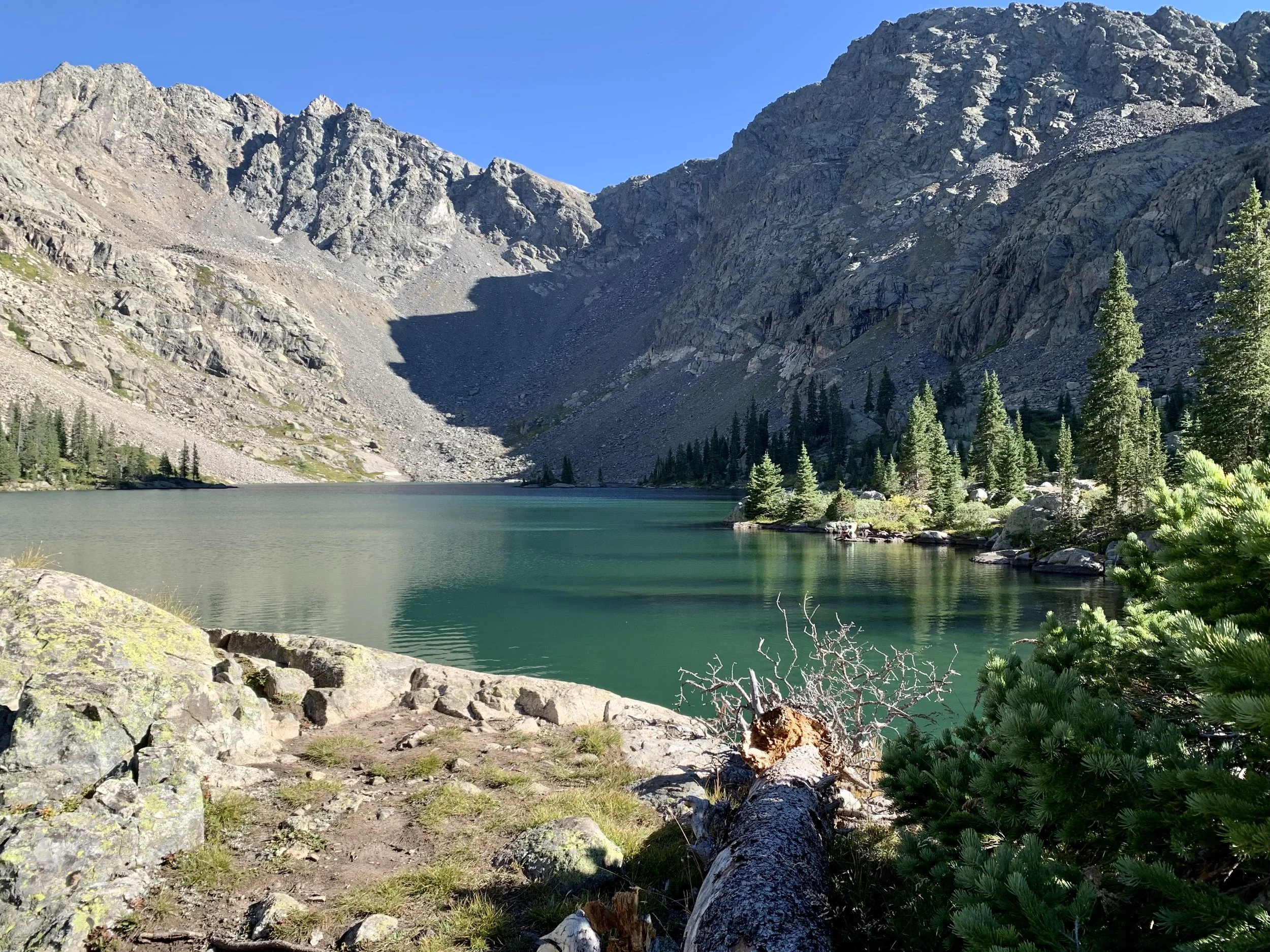 Serene alpine lake in Colorado surrounded by rocky peaks and pine forest under blue sky – symbolizing reflection, balance, and healing through nature-based therapy and counseling in Boulder and Lafayette.