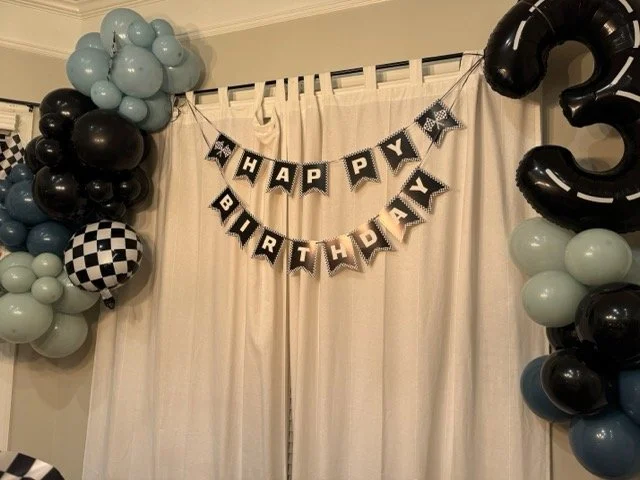 Happy Birthday banner, blue and black balloon garlands, a checkered round balloon, and a large black number 3 balloon demonstrating the SB Realty budget friendly party backdrop hack