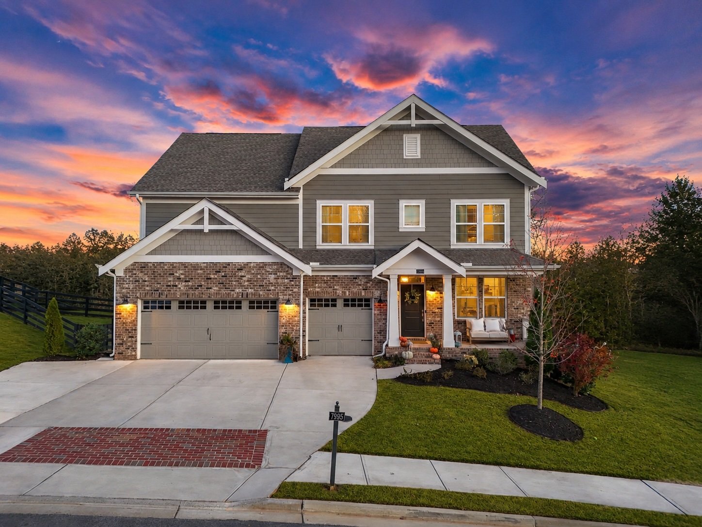 two-story home at 7995 Veranda Curve in Ball Ground, Georgia, featuring a brick and siding exterior, three-car garage, covered front porch, manicured landscaping, and a vibrant sunset sky. The property offers 4 bedrooms, 4.5 bathrooms,
