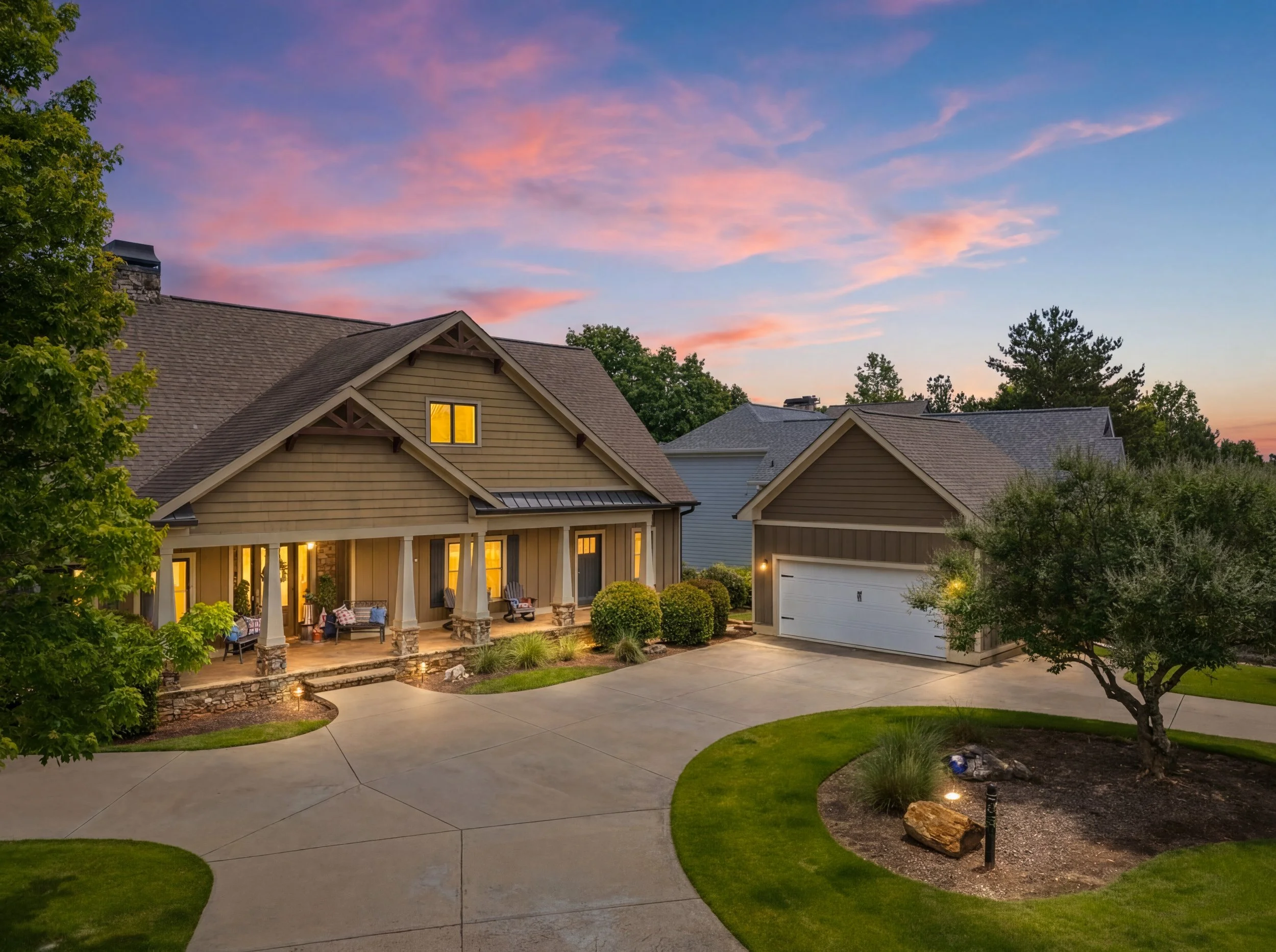 65 Cottage Lane in Toccoa, Georgia, featuring a beautifully maintained Craftsman-style home in Currahee Club with a covered front porch, detached two-car garage, manicured landscaping, and a curved driveway beneath a colorful sunset sky.
