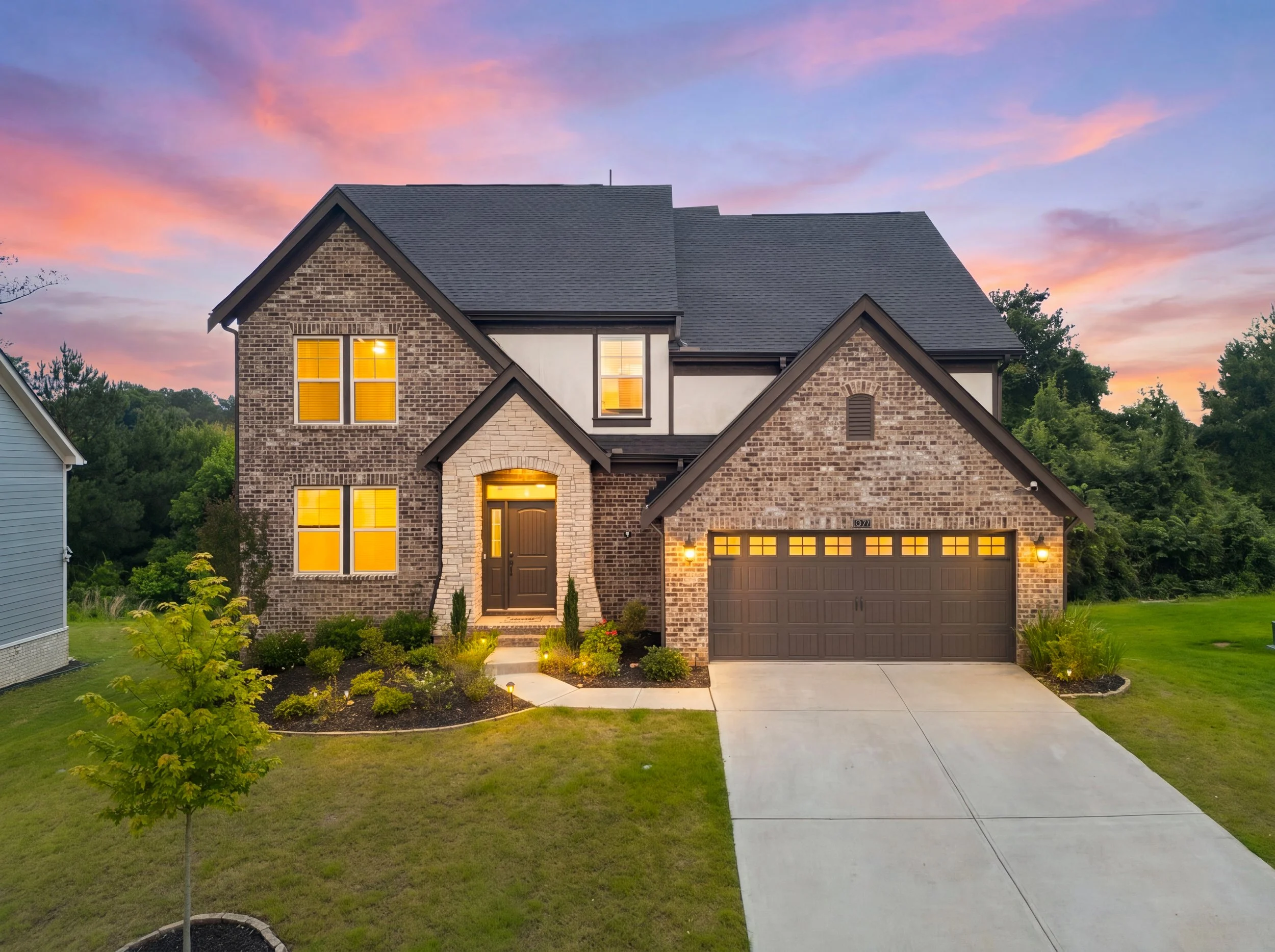 Twilight exterior of a two-story brick and stone home at 8150 Scenic Ridge Way in Ball Ground, featuring warm interior lighting, a covered front entry, attached garage, and landscaped front yard.