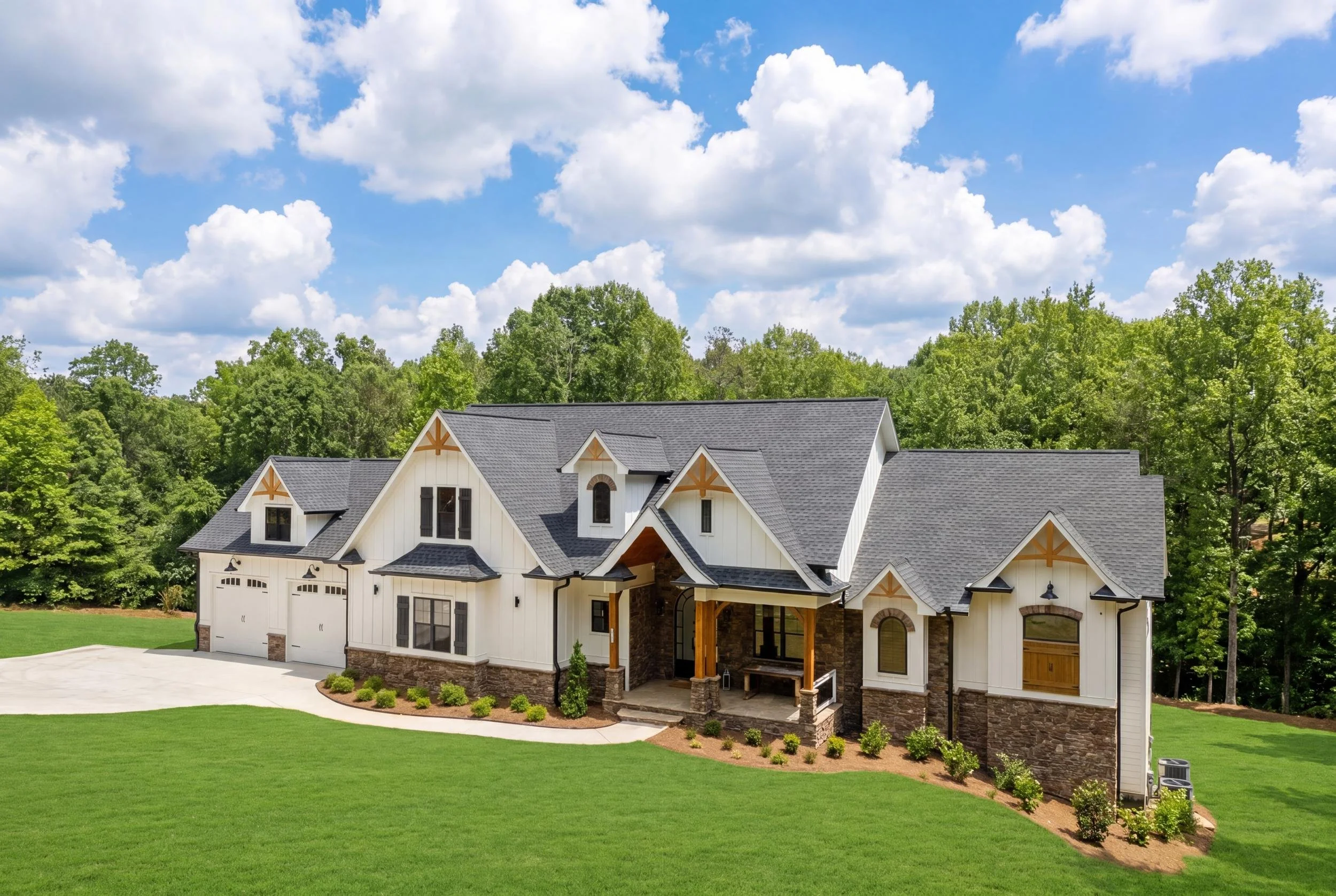 Exterior view of 101 Attwater Circle, a luxury new construction home in Crystal Falls, Dawsonville, Georgia, featuring craftsman architecture, stone accents, a covered entry, three car garage, and lush landscaping under a bright blue sky.
