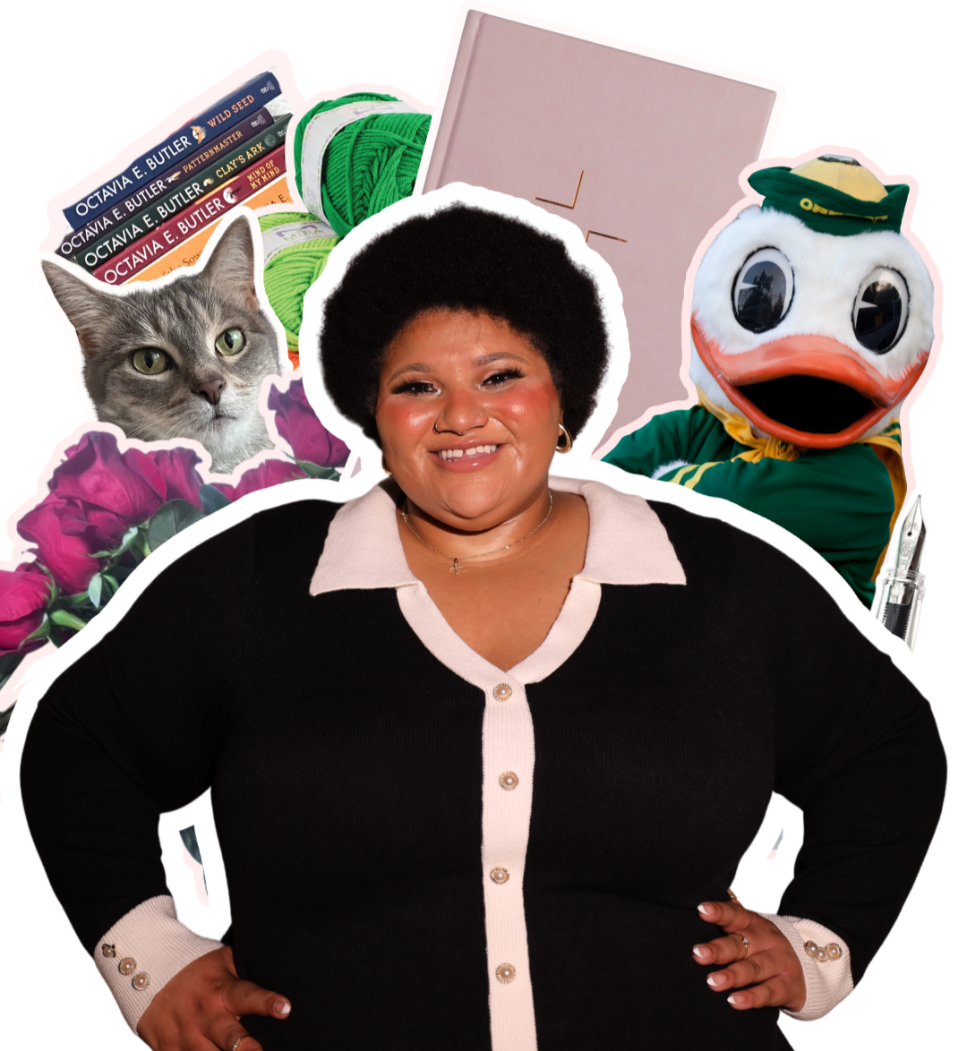 A woman with short, curly hair smiling, surrounded by a gray cat, a plush duck mascot, yarn balls, books, roses, a pink notebook, and a fountain pen.