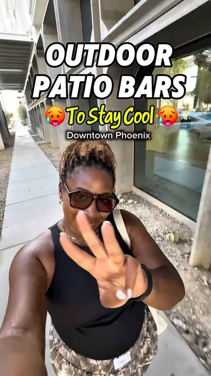 A woman taking a selfie outdoors on a sidewalk in downtown Phoenix, wearing sunglasses, a black top, and camouflage pants, with the text overlay "Outdoor Patio Bars To Stay Cool."