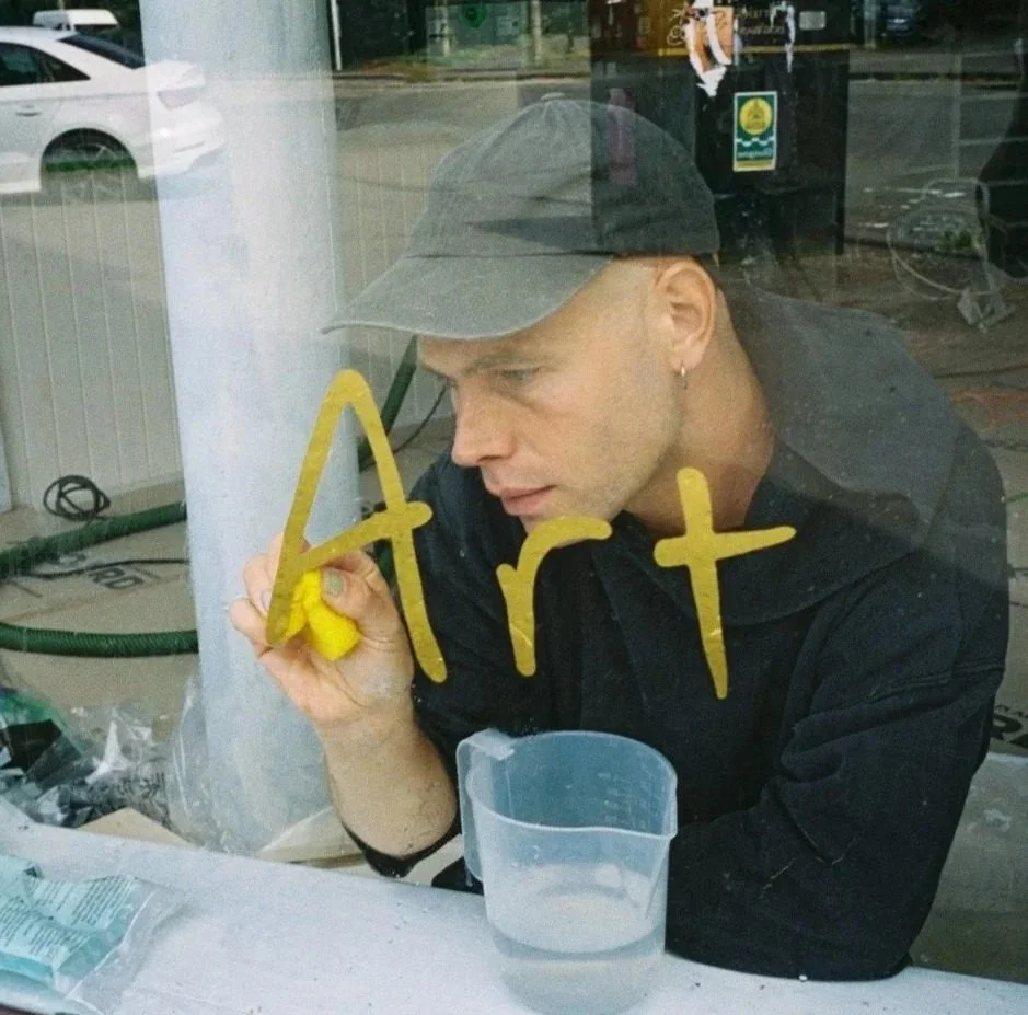 A signwriter applying gold leaf on a glass window, spelling out 'Art'.