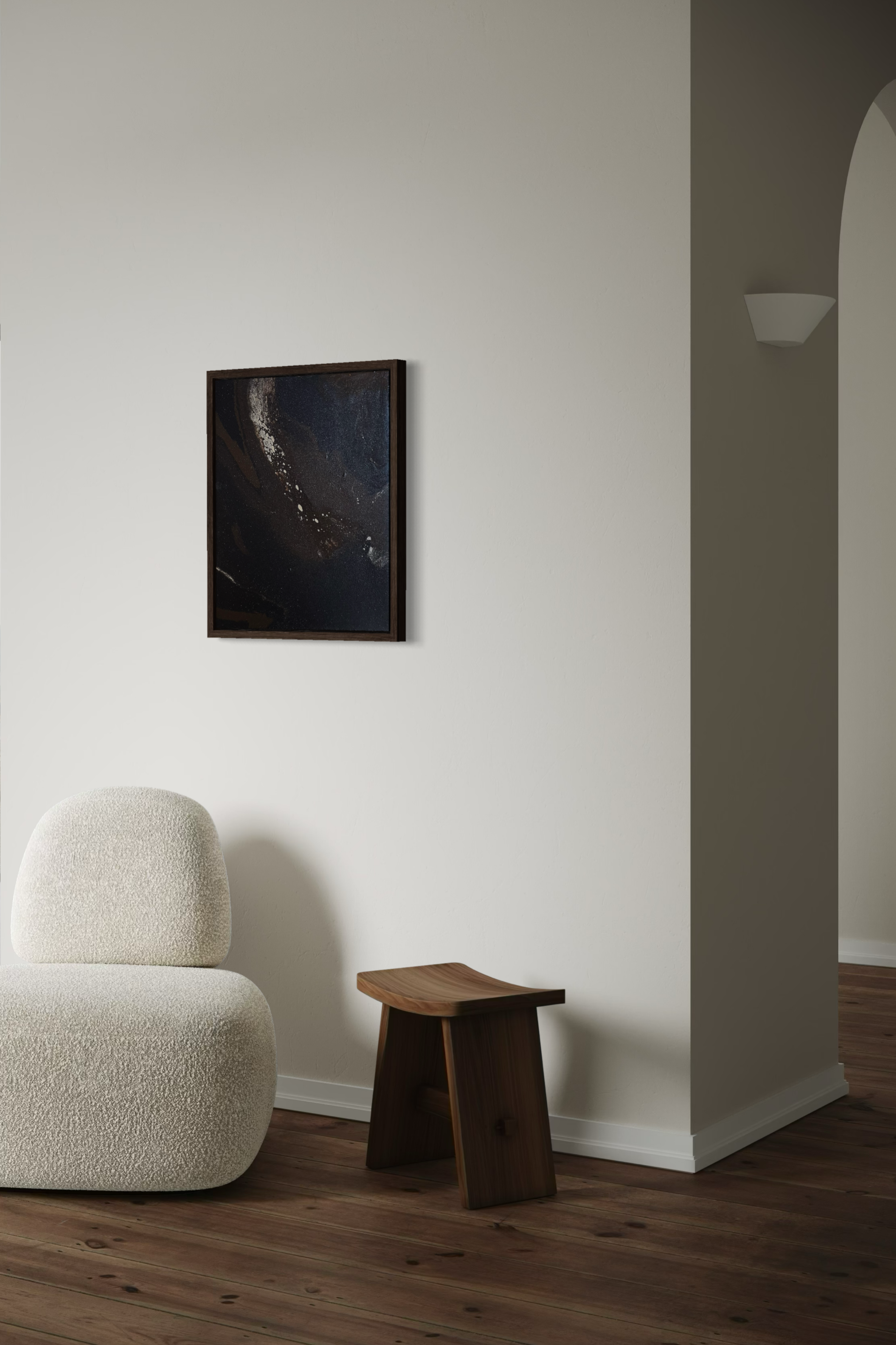 A living room corner with a textured white armchair, a small wooden side table, a framed abstract art piece on the wall, and a wall-mounted light fixture, with wood flooring and a partial view of a hallway with an arched doorway.