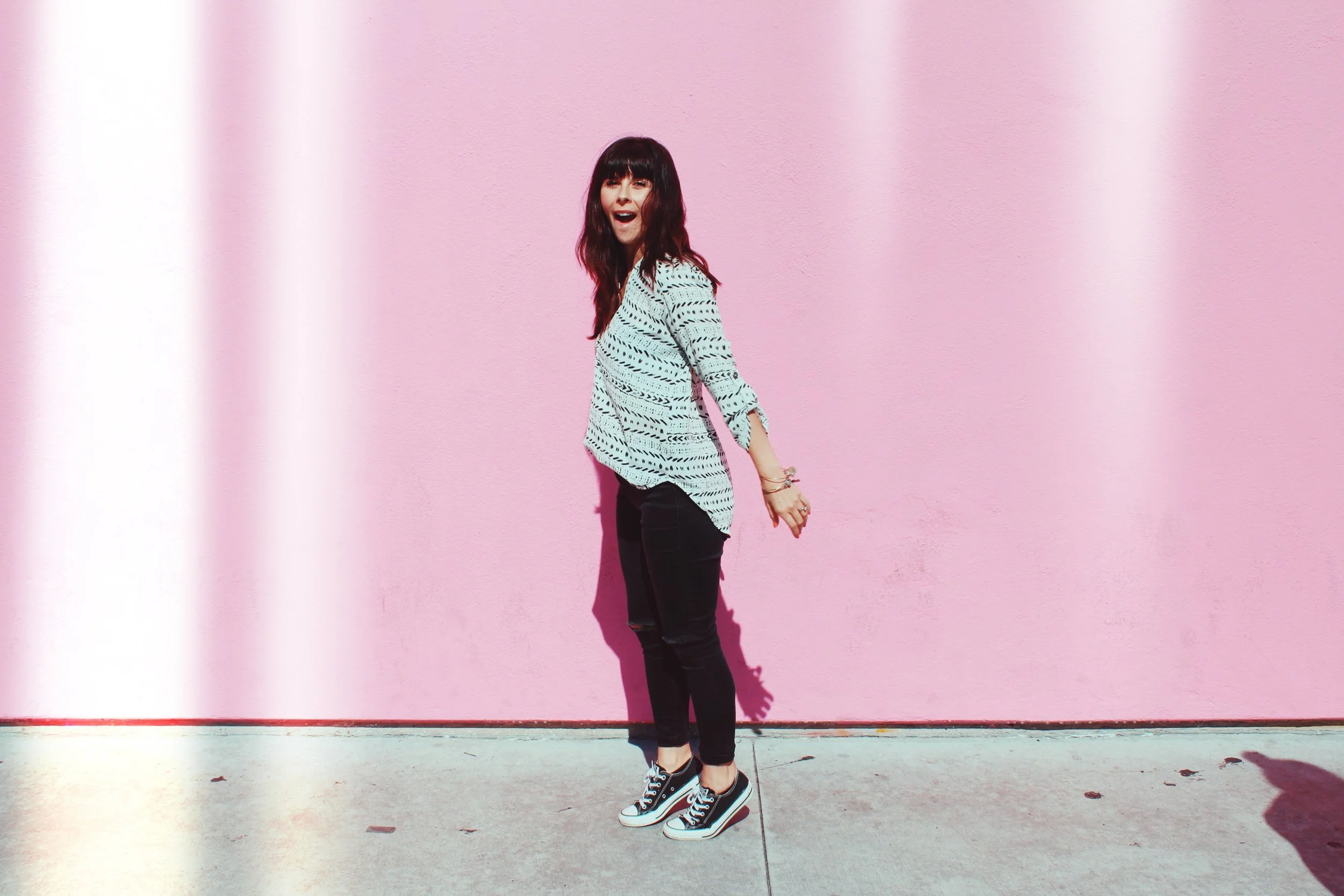 A woman standing in front of a pink wall with cute spring black jean outfit and black converse