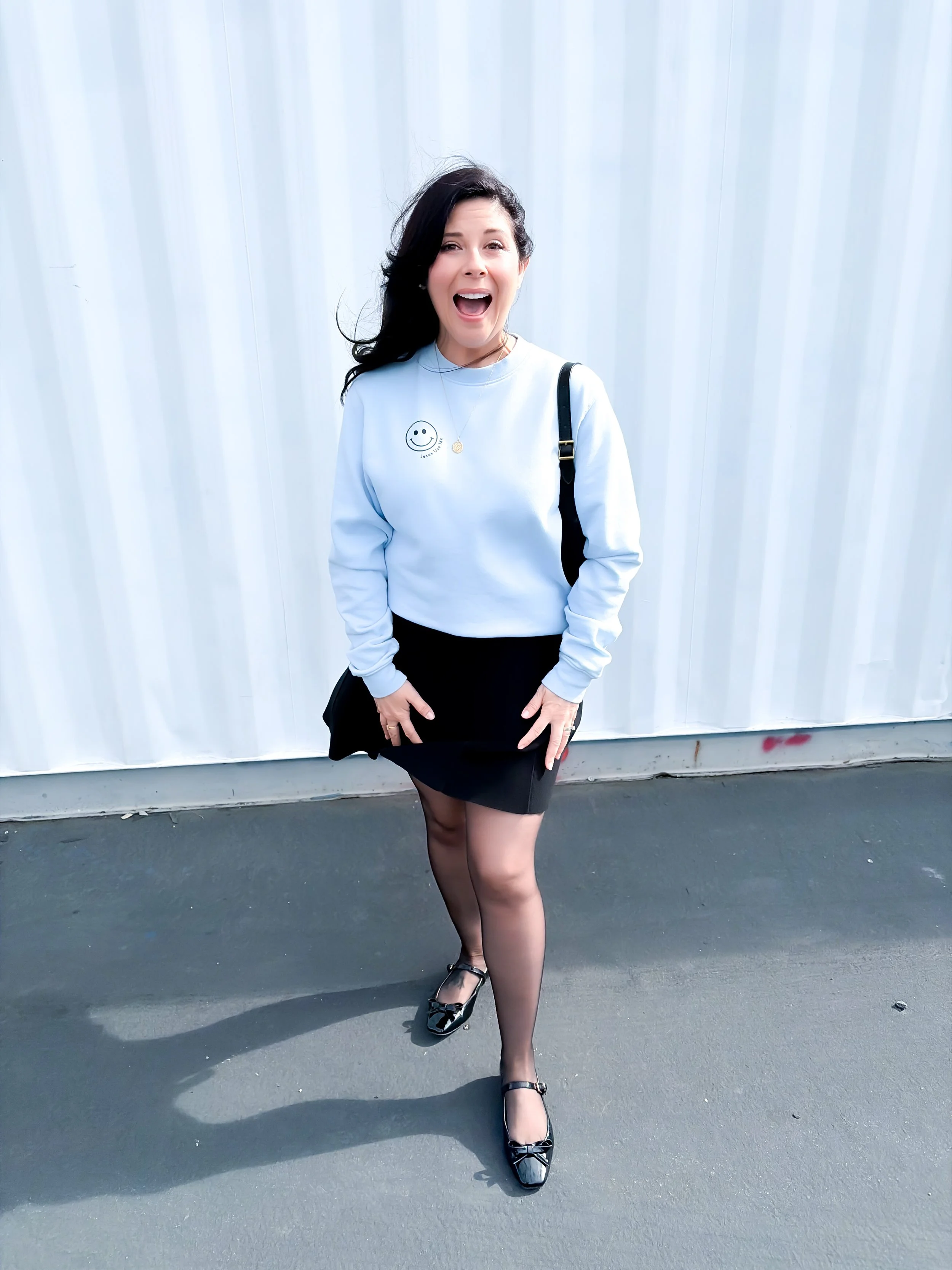 A classic spring outfit featuring a pastel blue crewneck sweatshirt, black skirt, and patent leather Mary Jane shoes.