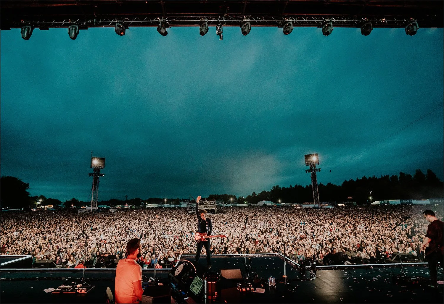 A large outdoor concert stage with musical performers and a crowd of attendees during evening.