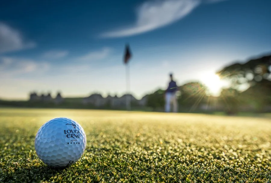 Close-up of a golf ball on the green with a person and flag in the background during sunset at Lough Erne Resort