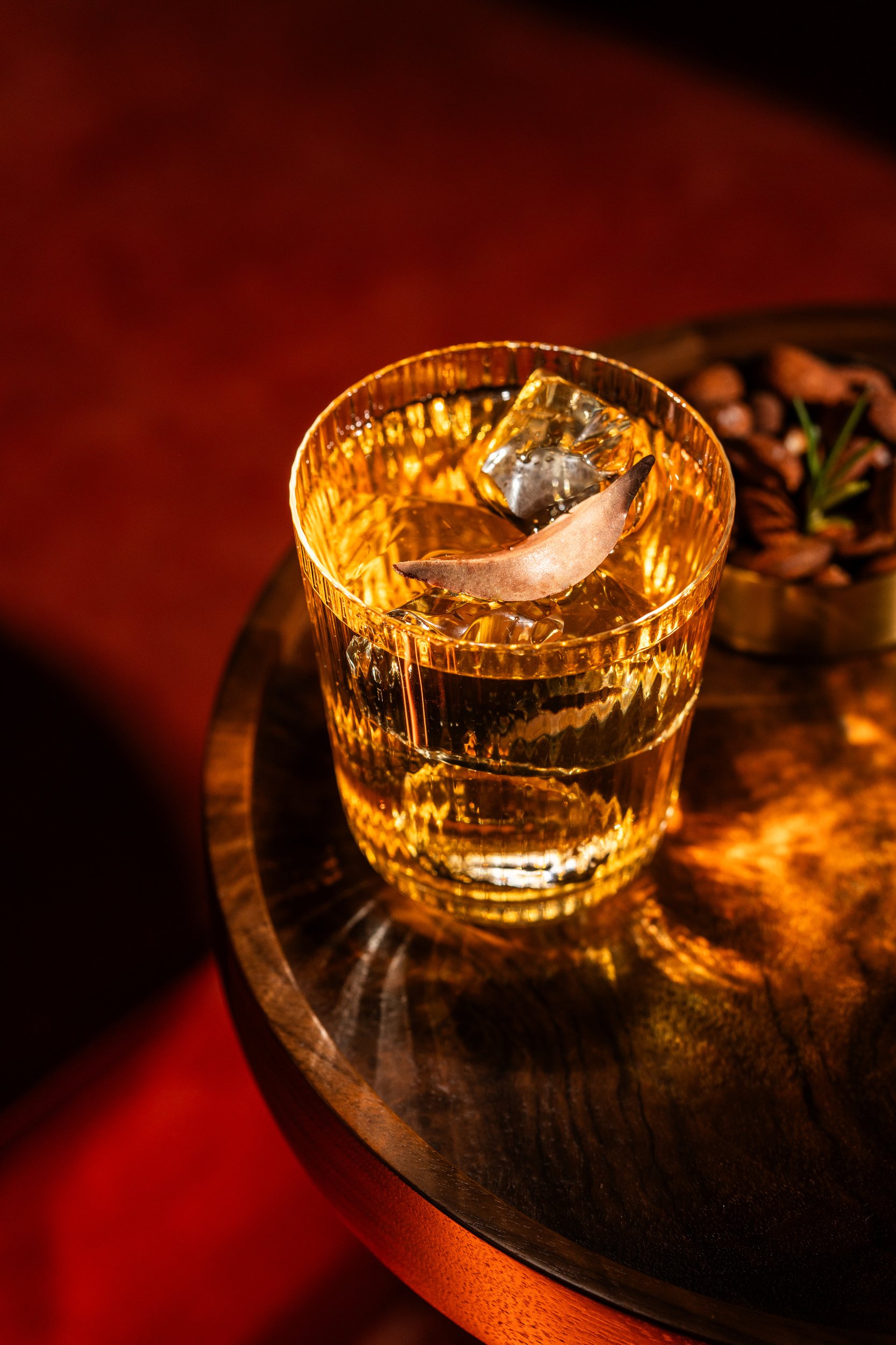 A glass of whiskey with ice and a lemon twist on a wooden table.