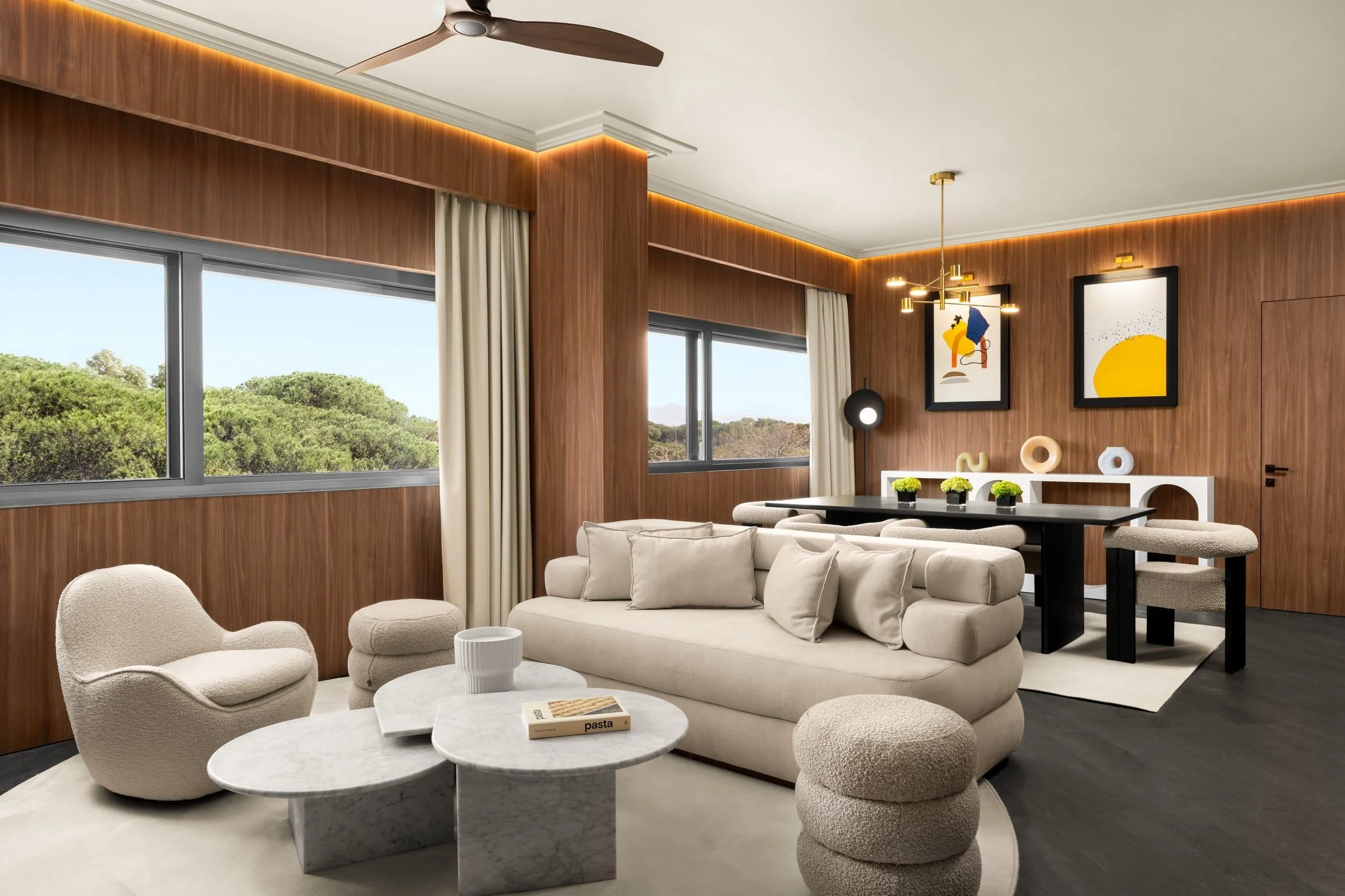 Modern Hotel room in Marriott Cardo Rome with beige sectional sofa, marble coffee tables, textured armchair, and cushioned stool. Large windows with white curtains, wood-paneled walls, and decorative artwork. 