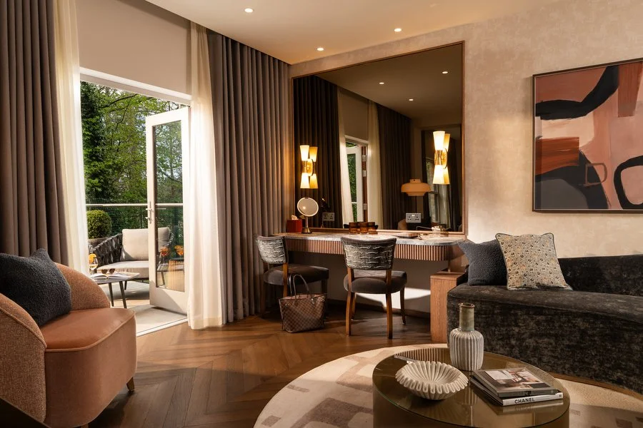 Luxurious hotel living room with large windows, a balcony, modern decor, a black velvet sofa, a round coffee table, and a wall art piece.