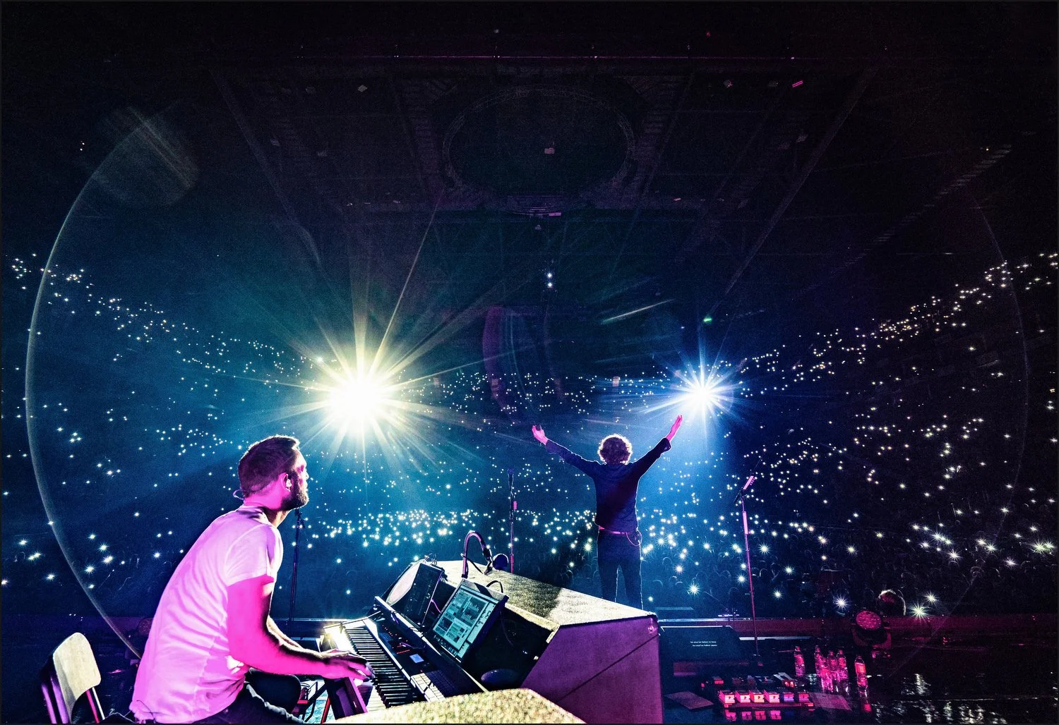 Musicians performing on stage with bright lights and an audience holding up light sticks.