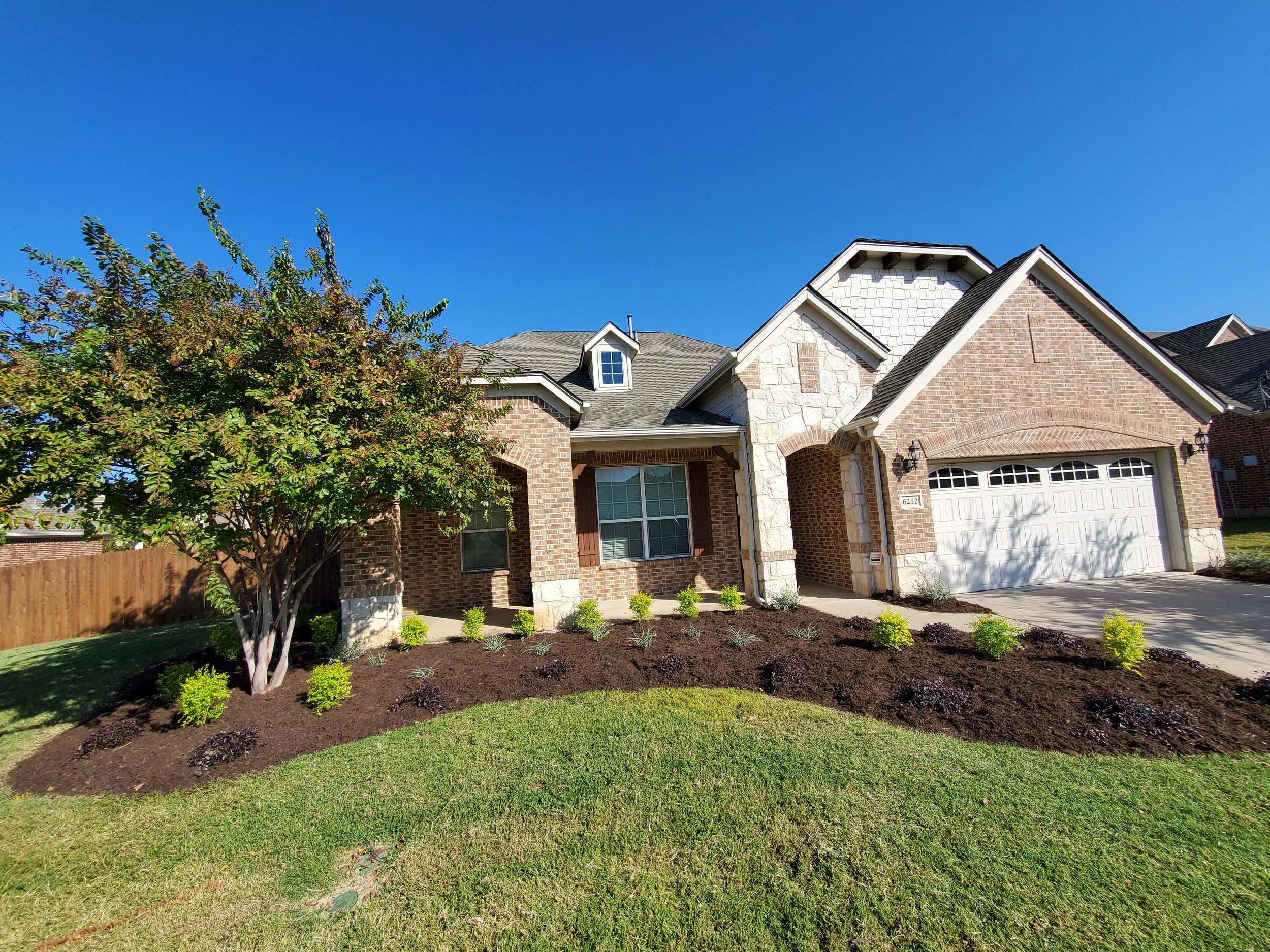 A front facing angle of a high contrast landscape installed by Designs of Eden, LLC that completely replaced the old overgrown front flowerbeds, giving year round curb appeal.