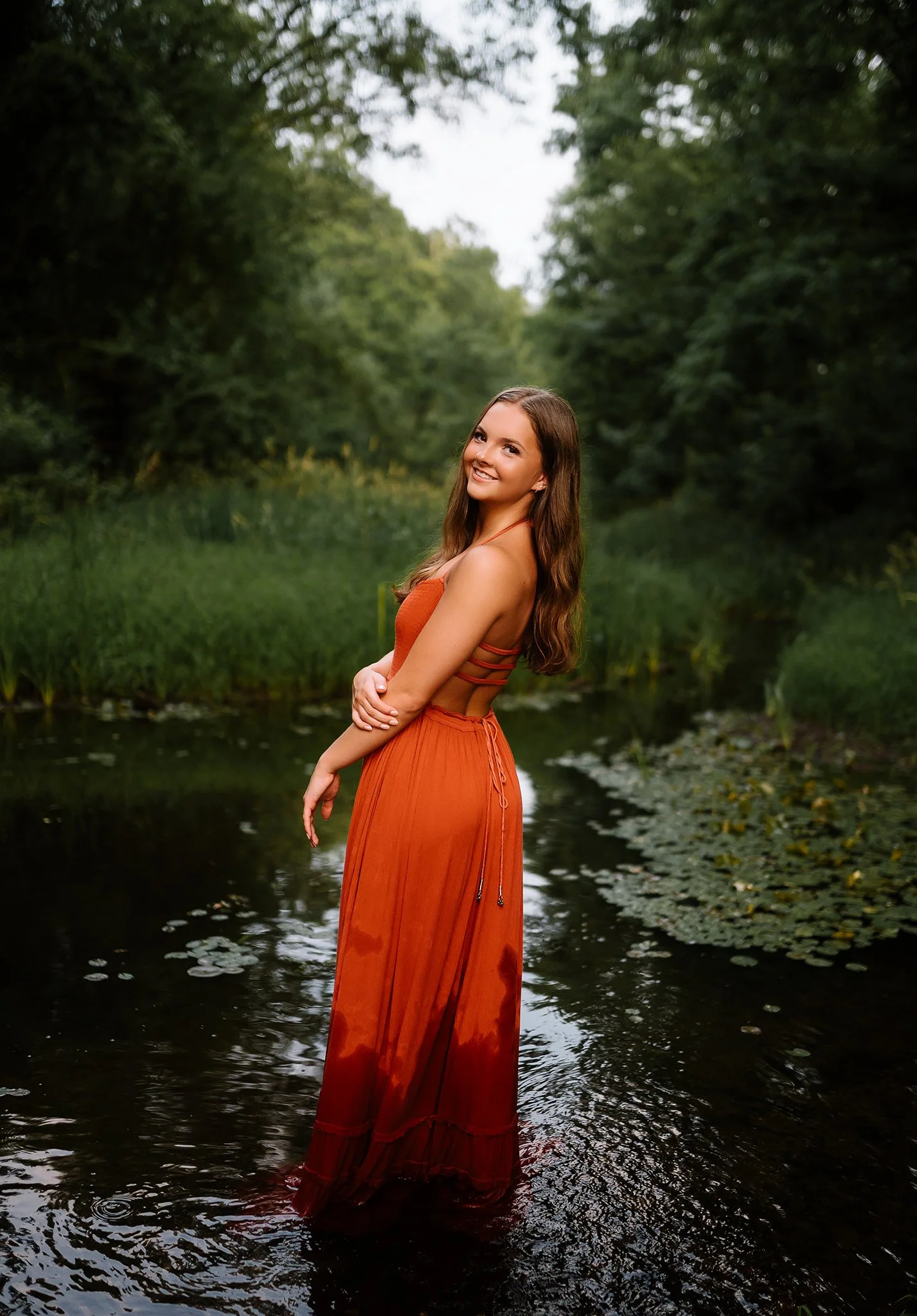 Senior photography session showing candid, relaxed posing style in water of dancer in orange dress