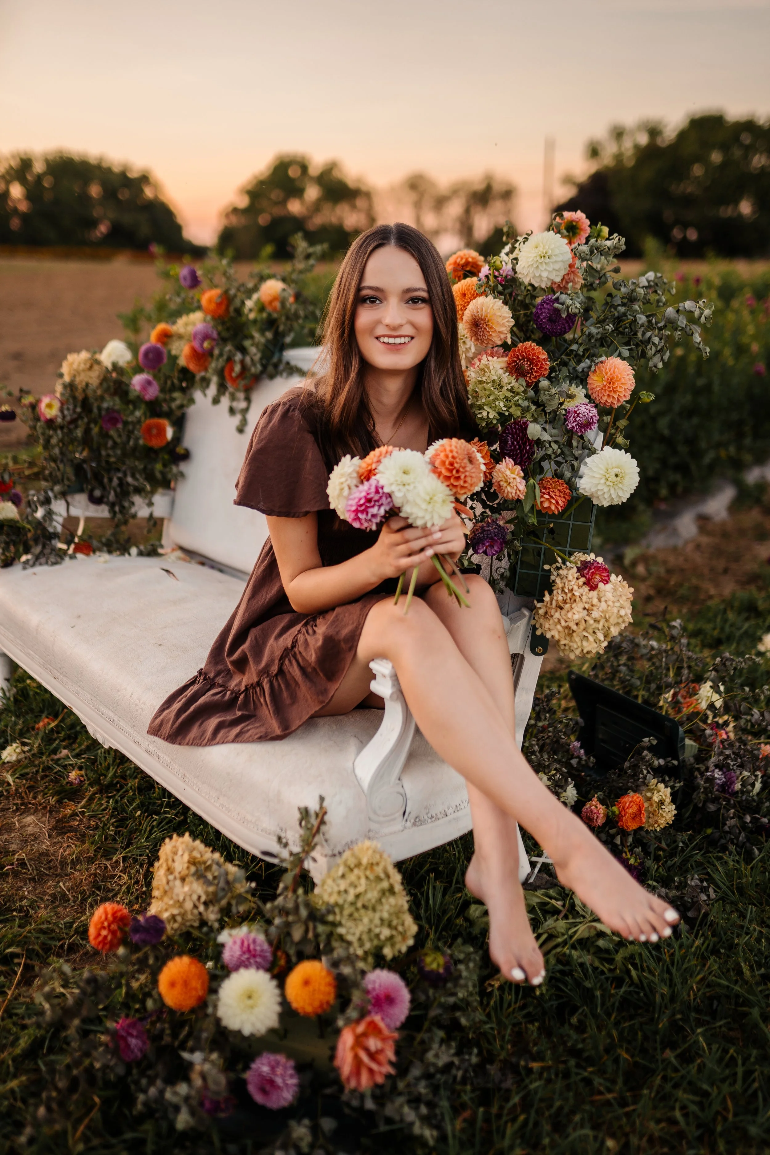 Young woman a senior in highschool sitting on a floral bench at sunset smiling at the camera. Canal Fulton Ohio family photographer luxury outdoor session