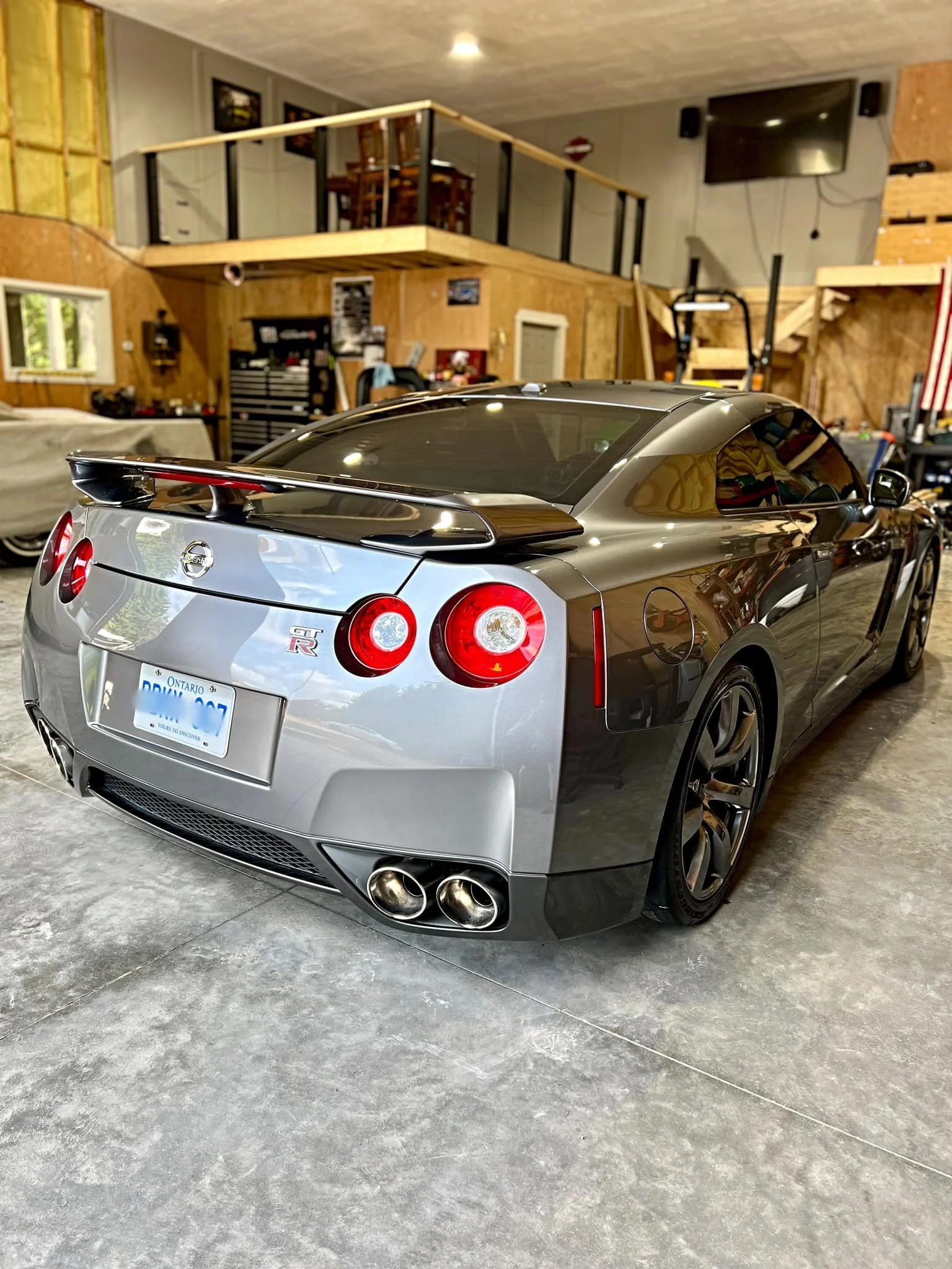 Silver Nissan GT-R sports car parked inside a garage with a wooden interior and various tools and furniture.