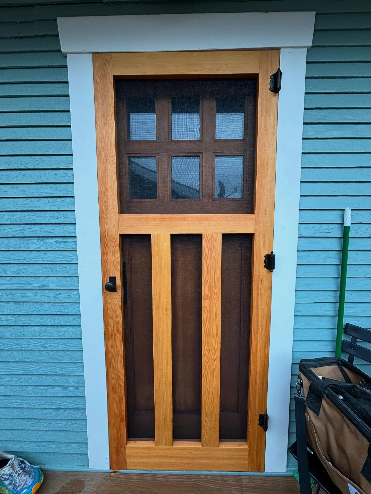 Built to match and made to fit. This screen door was crafted with tall mullions to mirror the six-pane window behind it and carefully installed inside a deep jamb with a slight bow at the top. The natural wood tones against the cool blue siding make