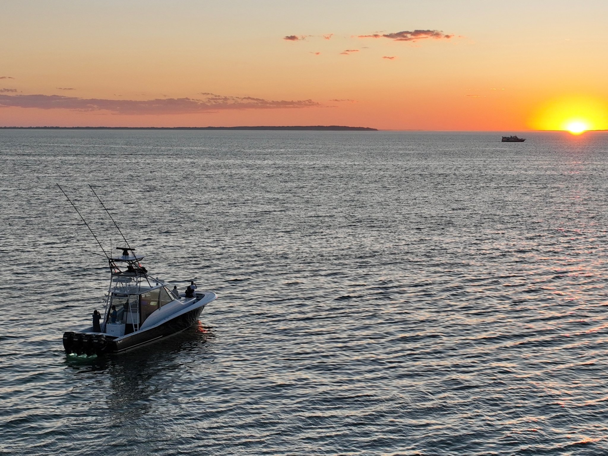 A boat on the water during sunset with a colorful sky and the sun near the horizon.