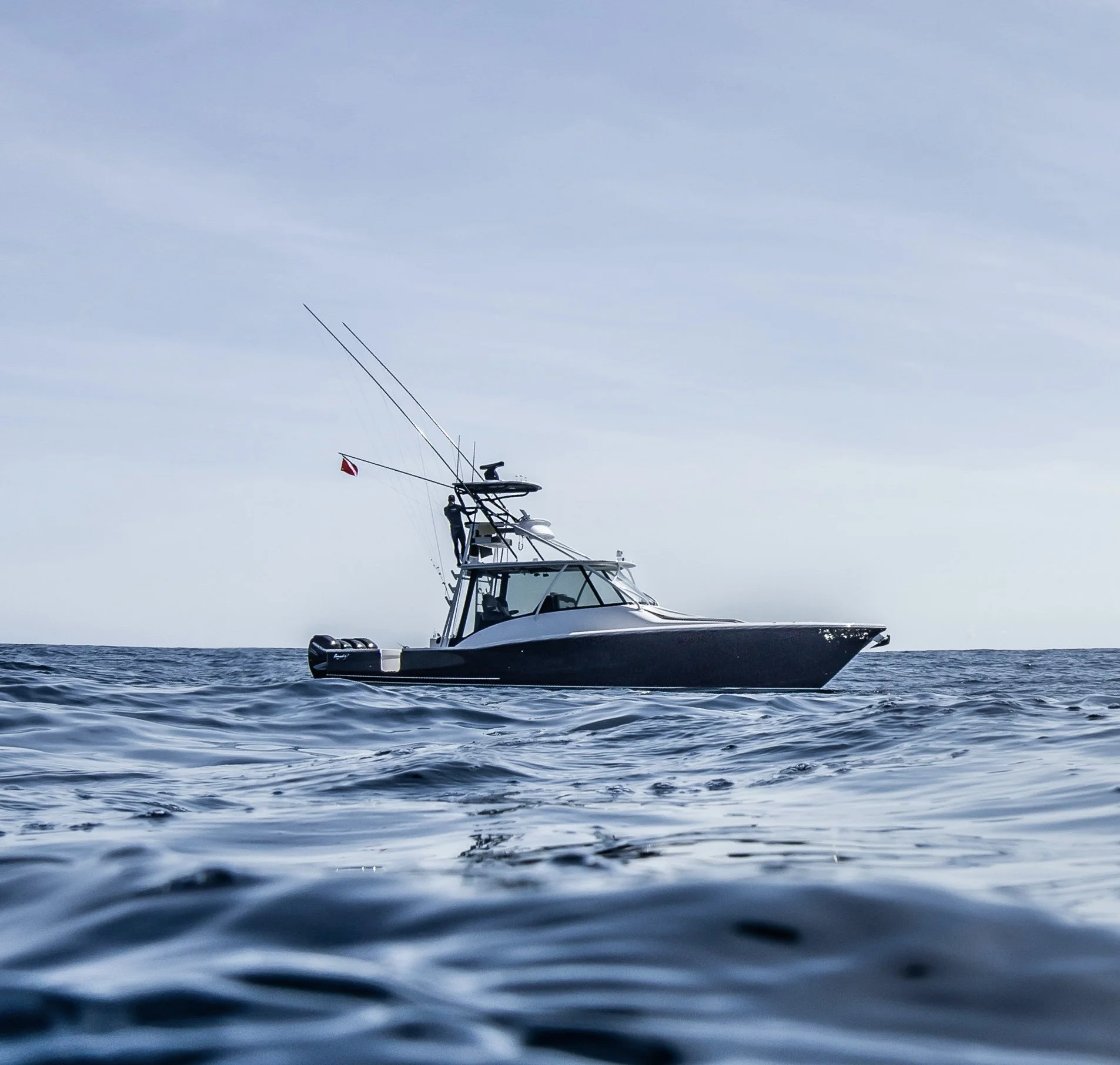A sleek black and white motorboat floating on calm ocean waters with a boat controller and fishing rods on the deck under a partly cloudy sky.