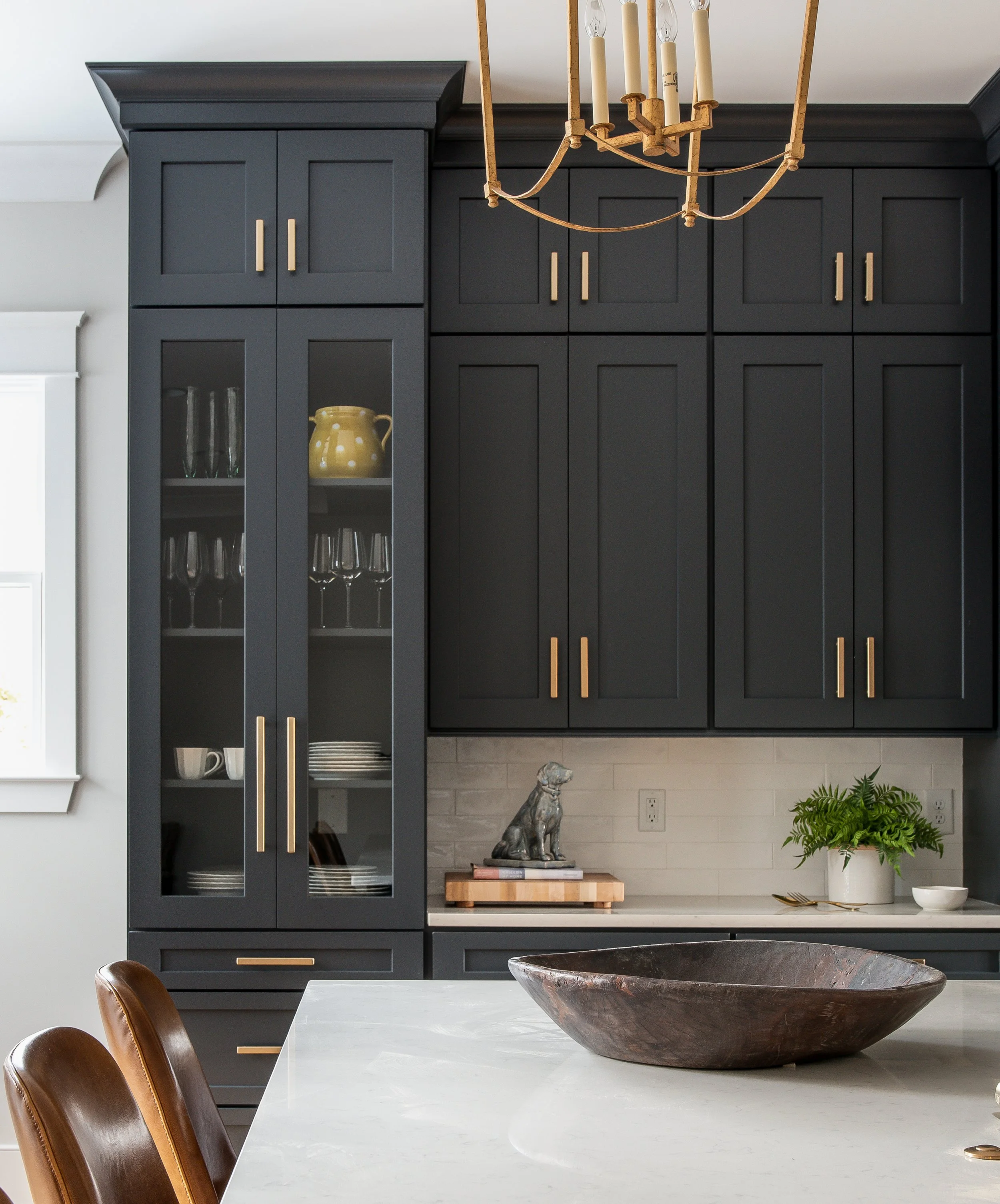 Modern black shaker cabinets with creamy countertops, brushed gold hardware and glass doors.