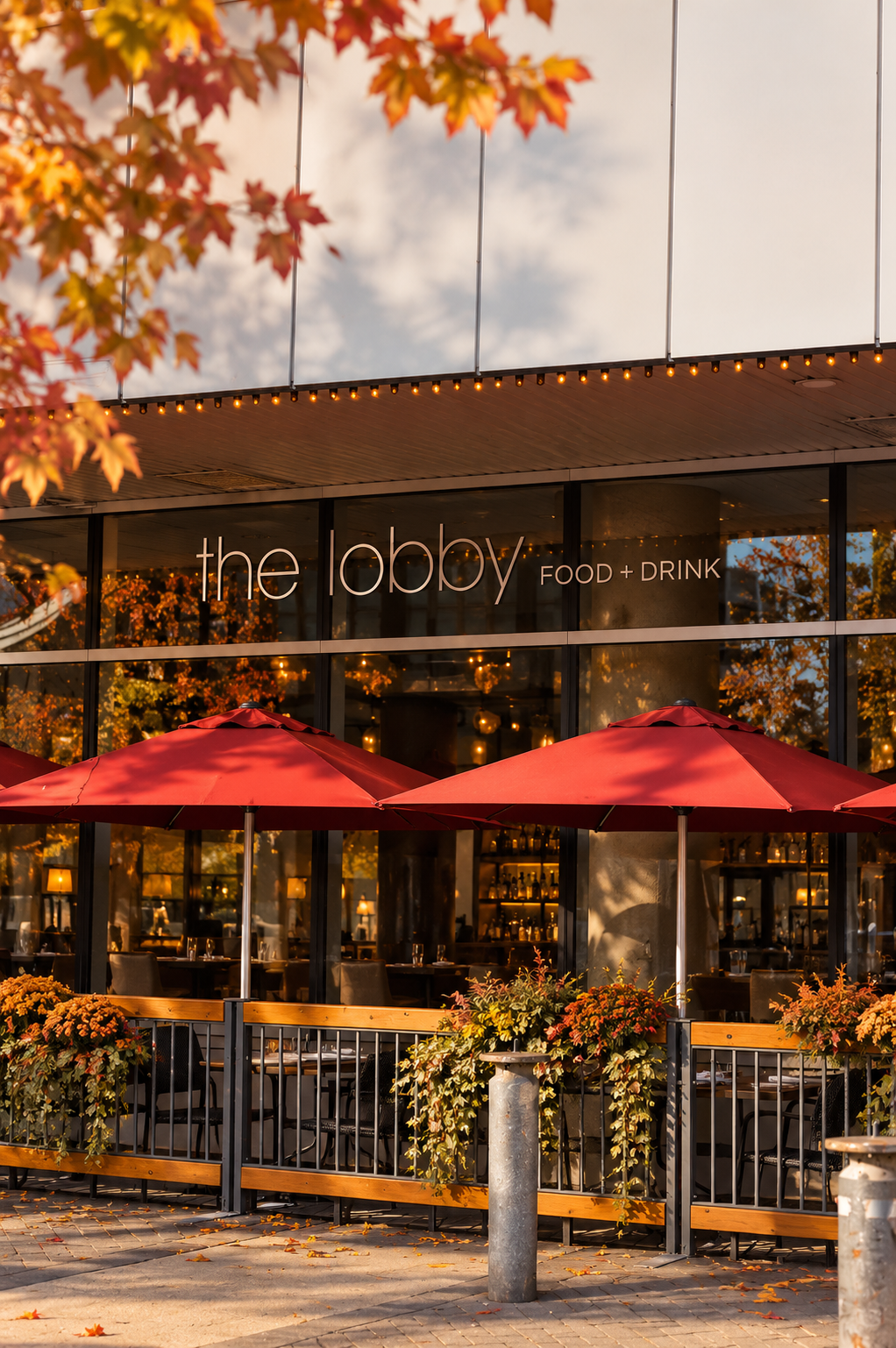 The lobby food and drink restaurant exterior with red patio umbrellas, autumn foliage, and outdoor seating.