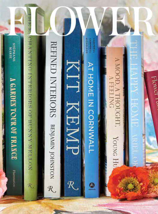 A collection of colorful books standing upright on a surface, with a few orange flowers in front of them.