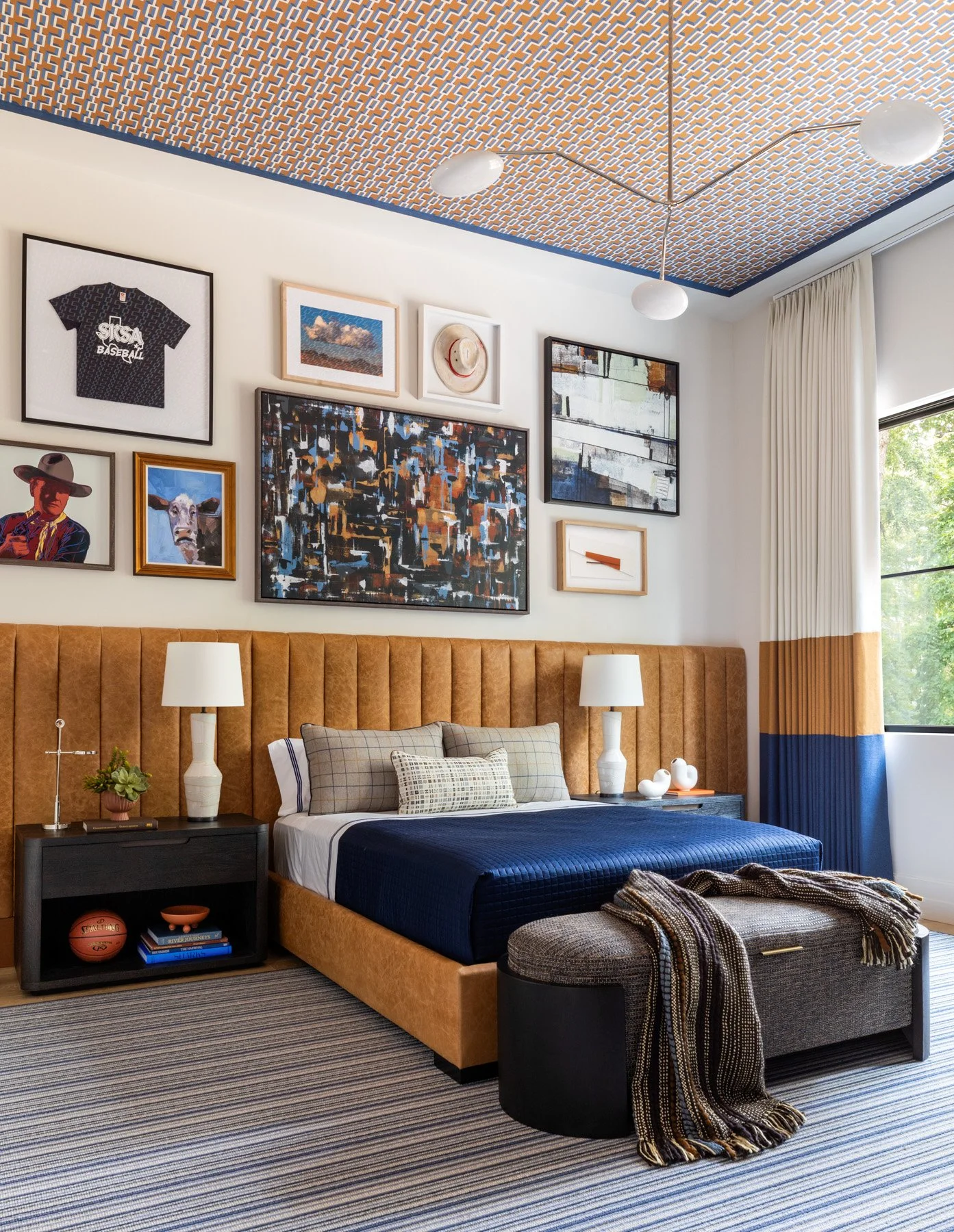 Benjamin Johnston Design Houston luxury interior design and architecture — boy's bedroom with caramel upholstered headboard wall, patterned ceiling wallcovering, gallery wall art collection, and navy blue color scheme.
