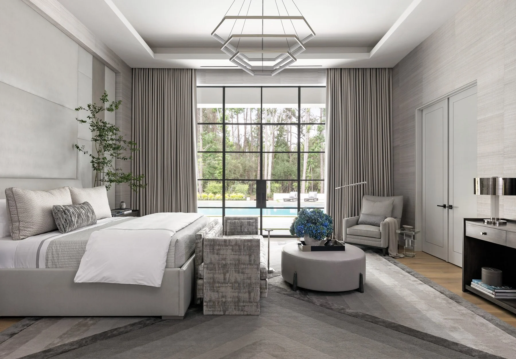 Benjamin Johnston Design Houston luxury interior design and architecture — primary bedroom with upholstered headboard wall, geometric chandelier, Chaddock Marco daybed, Chaddock Benito drink table, steel casement doors, and pool views.