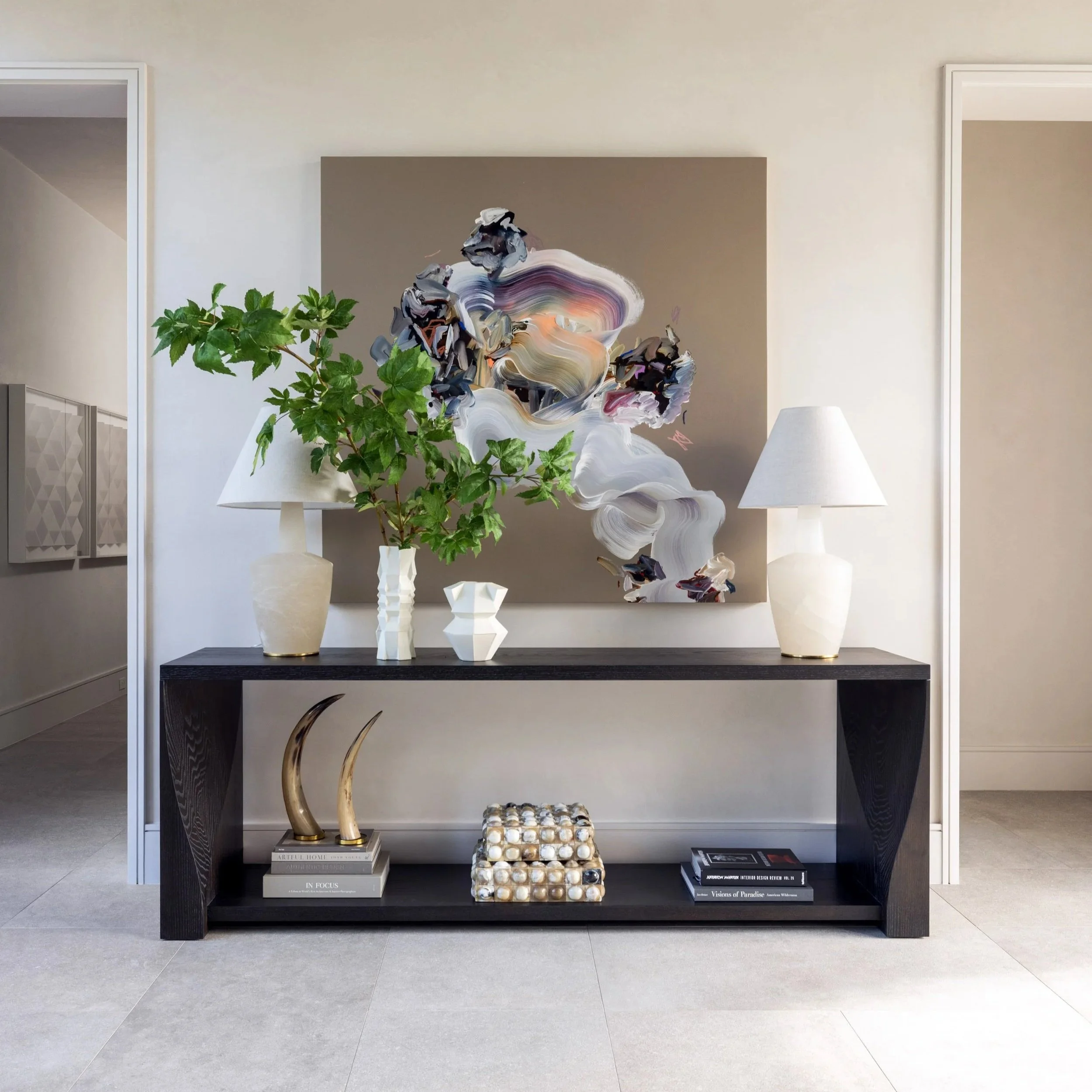 Benjamin Johnston Design Houston entryway featuring dark console table with abstract artwork, white ceramic lamps, sculptural vases, brass horn accent, and large scale botanical arrangement.