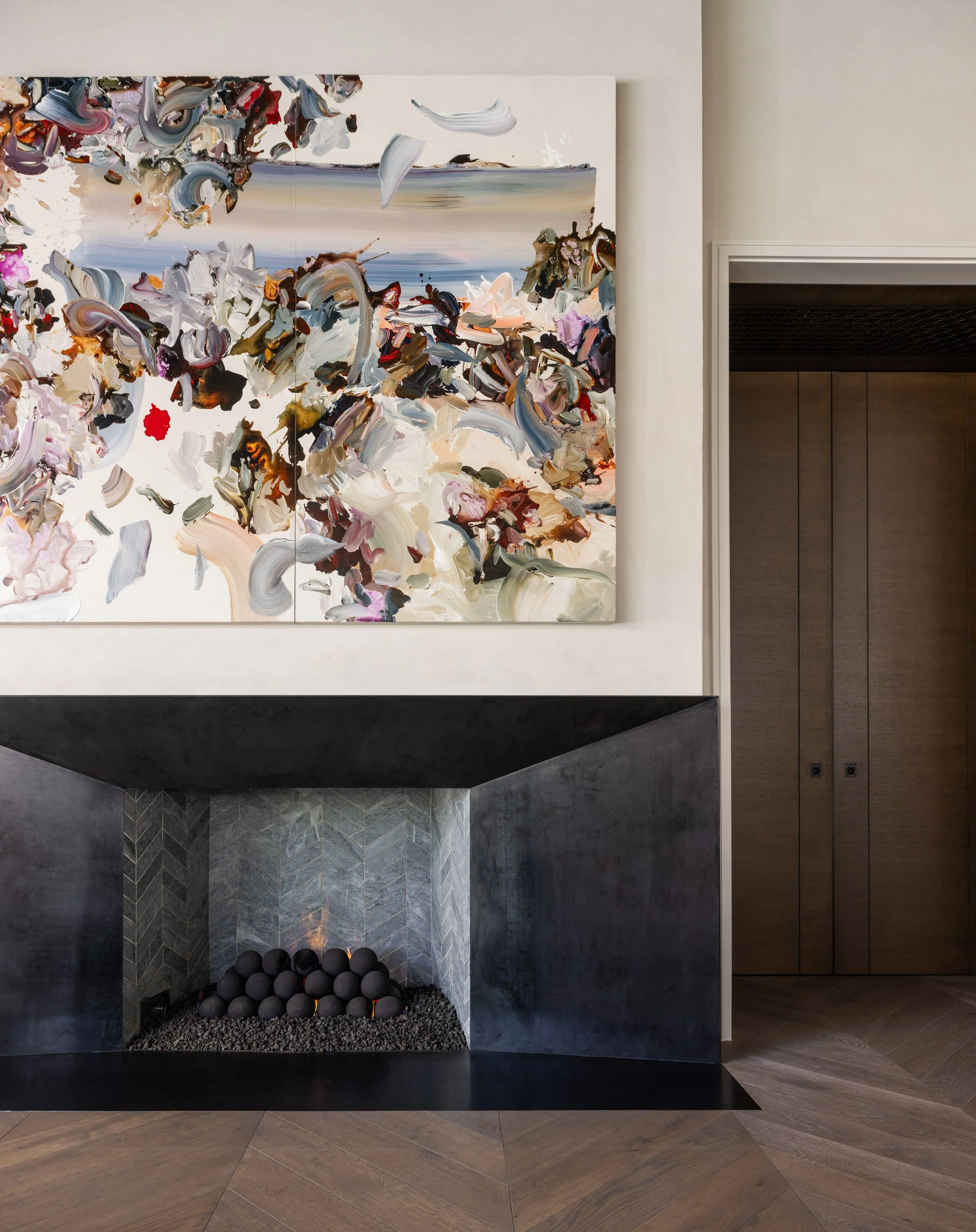 Benjamin Johnston Design Houston living room fireplace featuring dark sculptural surround with chevron tile firebox, large scale abstract artwork, and herringbone wood floor.