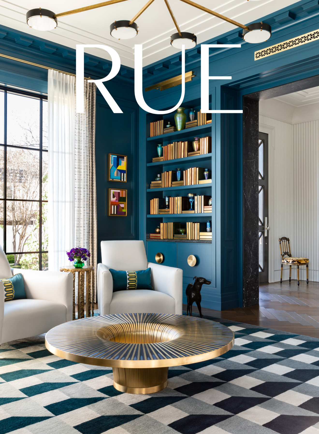 Benjamin Johnston Design Houston living room featured in Rue Magazine featuring deep teal paneled walls, built-in bookshelves, brass sunburst coffee table, white lounge chairs, and geometric rug.